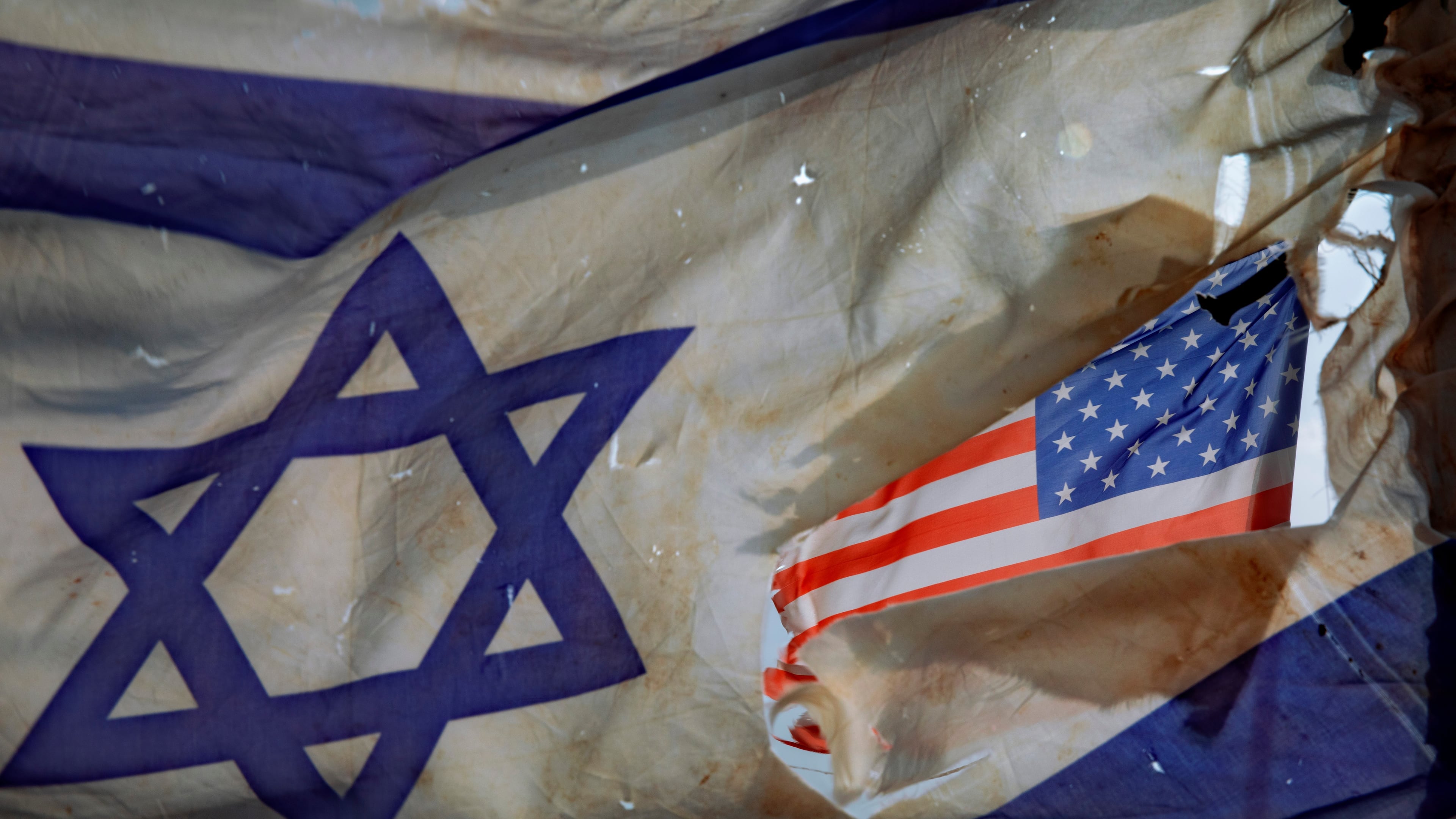 FILE- A U.S. flag is seen through a hole torn in an Israel national flag, as they wave in the wind at a horse ranch, near the southern Israeli town of Sderot, Friday, Nov. 20, 2020. (AP Photo/Oded Balilty, File)