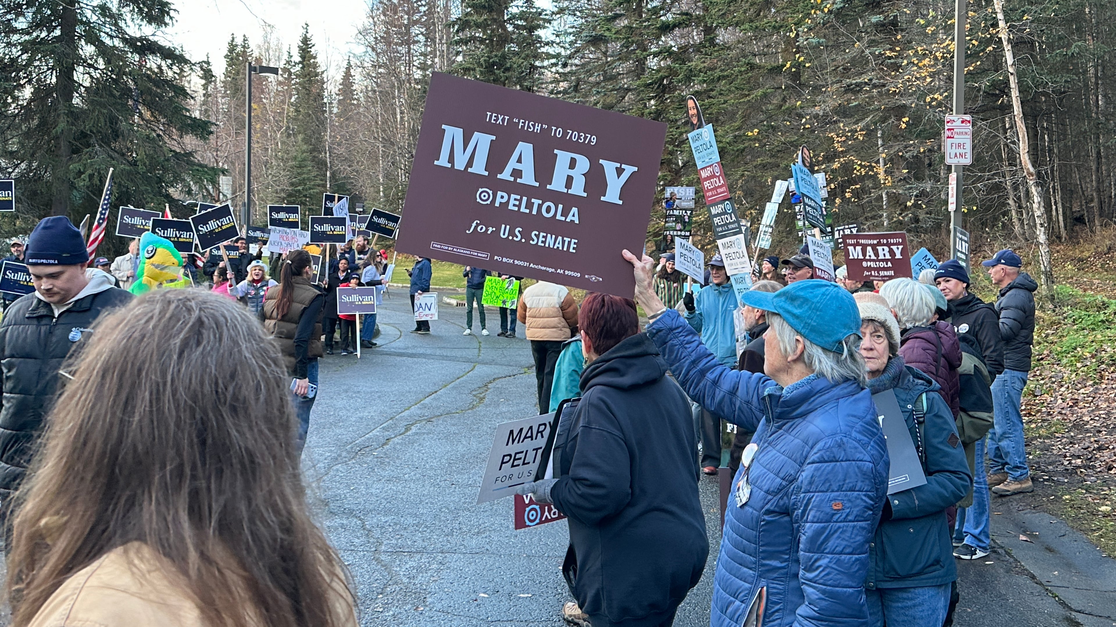 In this photo shot with a smart phone, supporters of Republican U.S. Sen. Dan Sullivan and Democrat Mary Peltola gathered outside the venue where the candidates were set to debate, Thursday, Oct. 15, 2026, in Anchorage, Alaska. (AP Photo/Becky Bohrer)