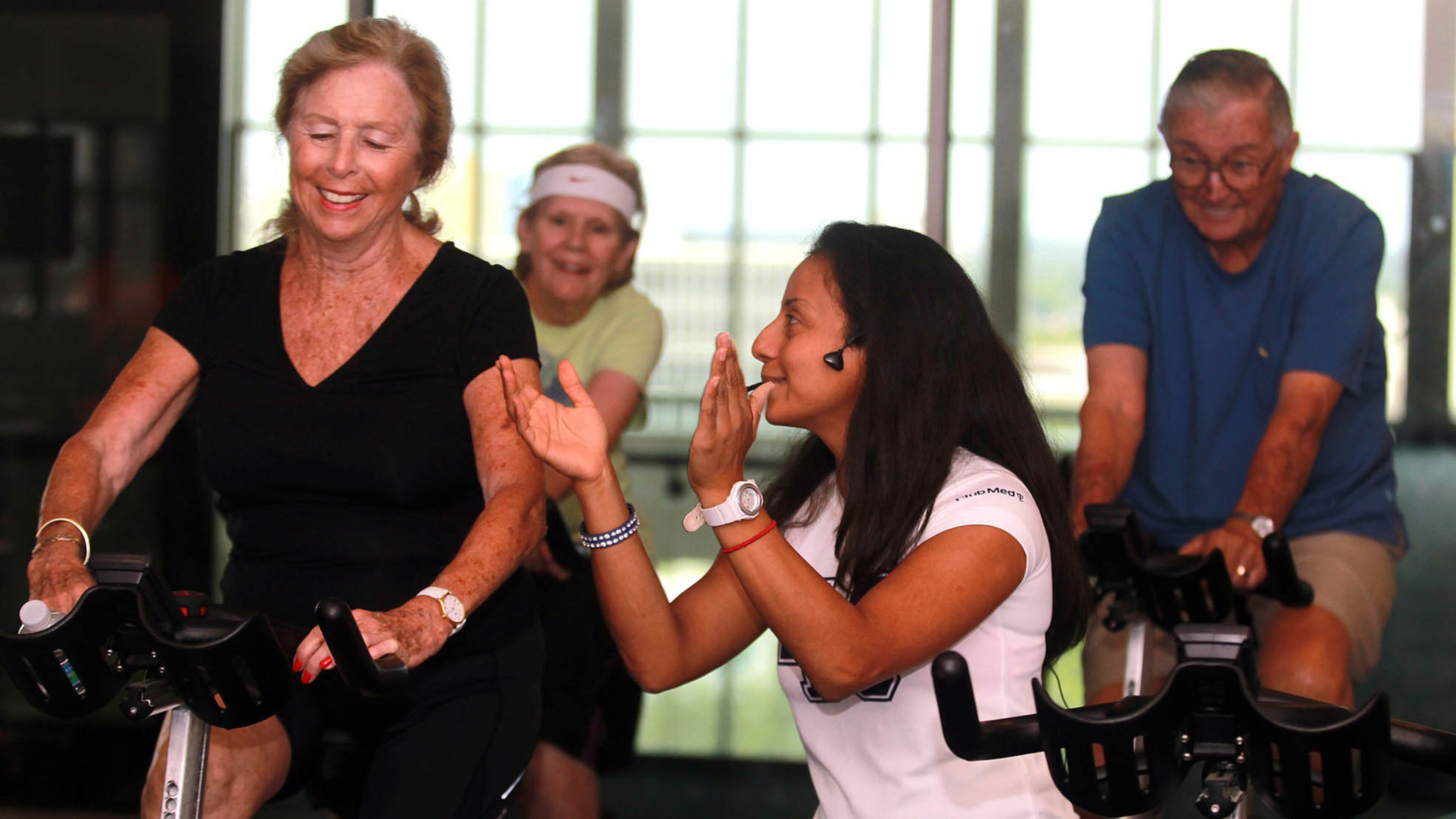 Angela Alvarado, a health coach instructor, helps Patricia Henning, left, during a cycling class for individuals with Parkinson's on Aug. 13, 2015.