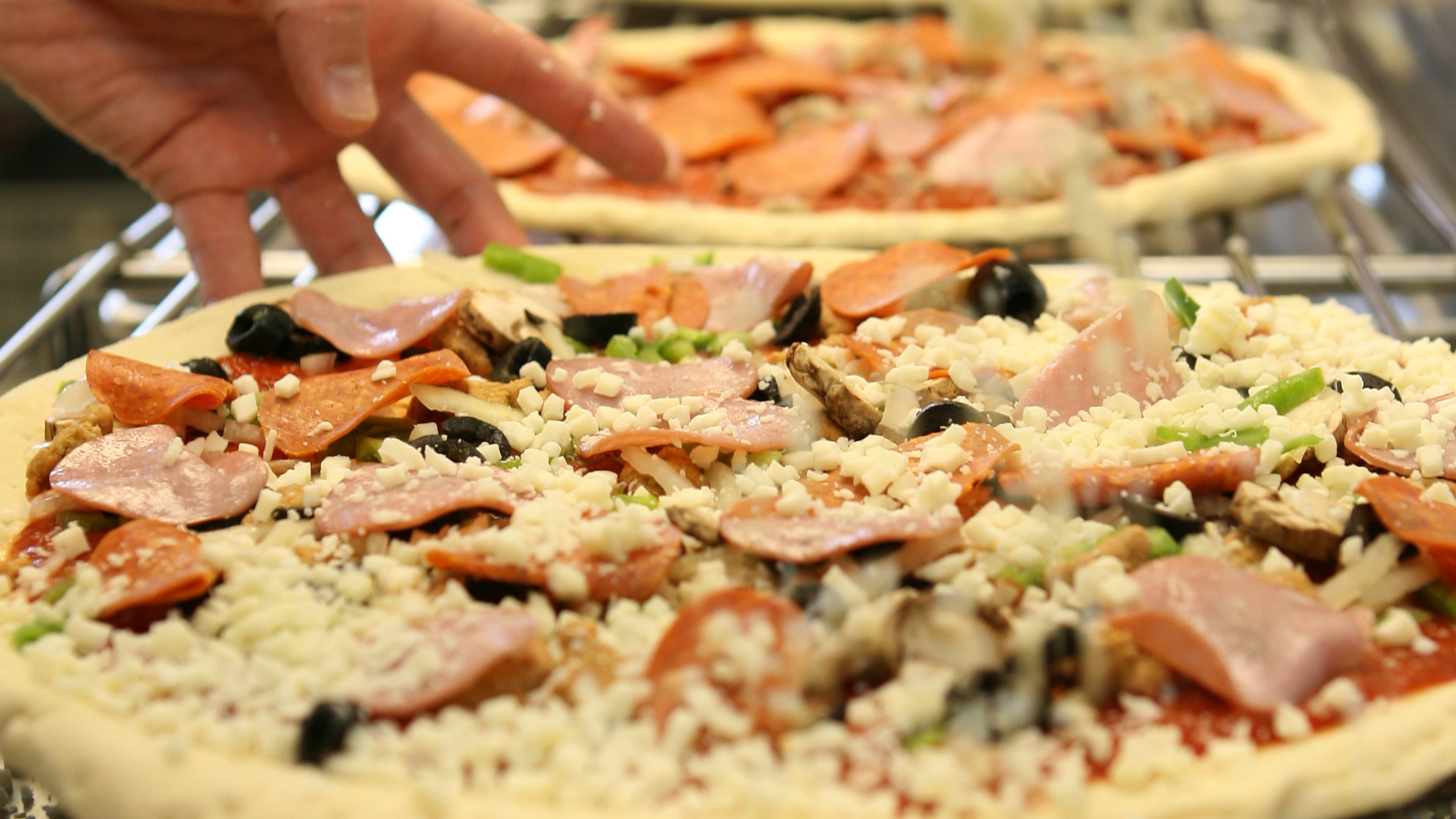A Papa John's manager tops off a pizza with some cheese during the Friday lunch hour. (Alison Church/Special)