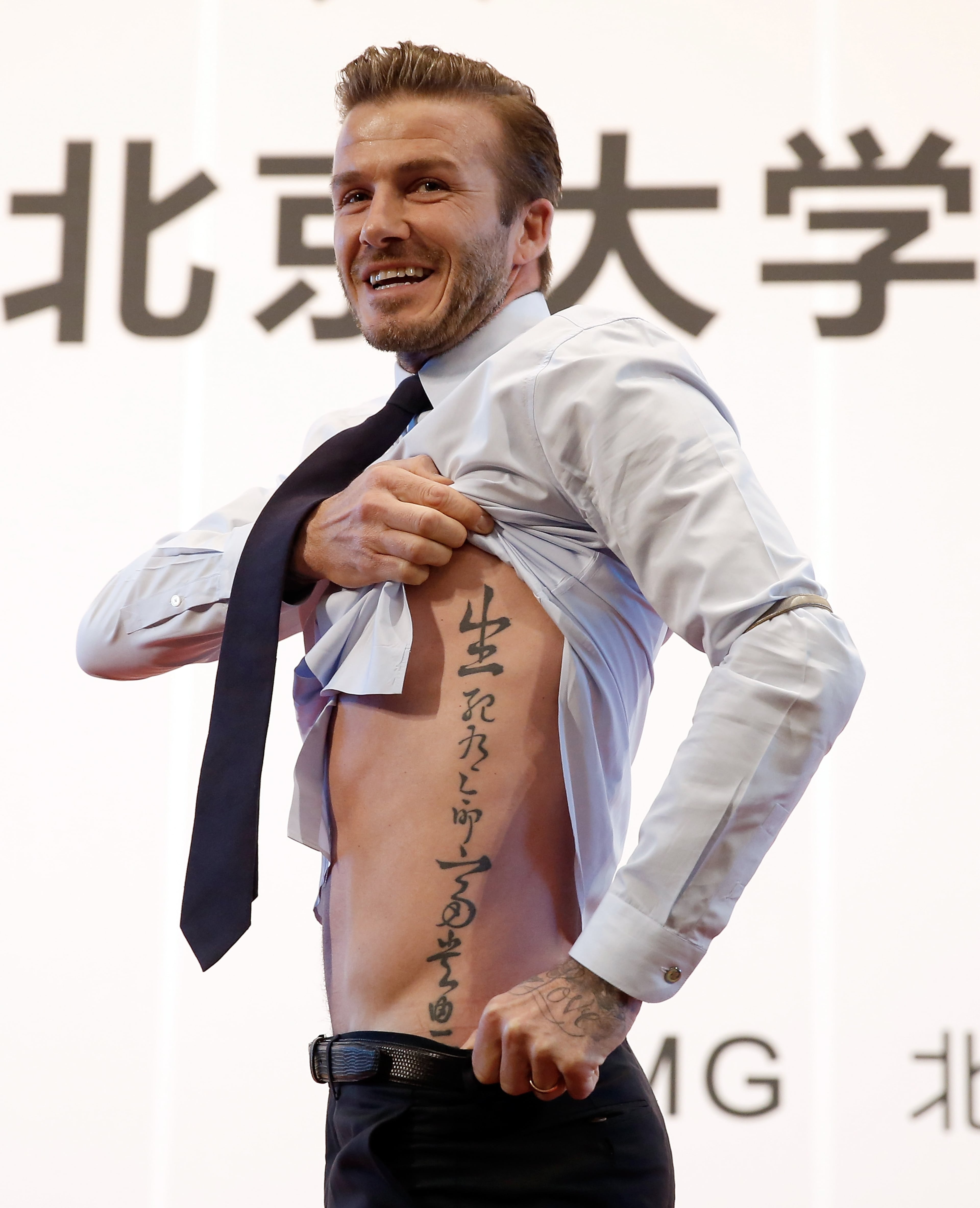 British football player David Beckham shows his tattoo to fans during his visit to Peking University on March 24, 2013, in Beijing, China.