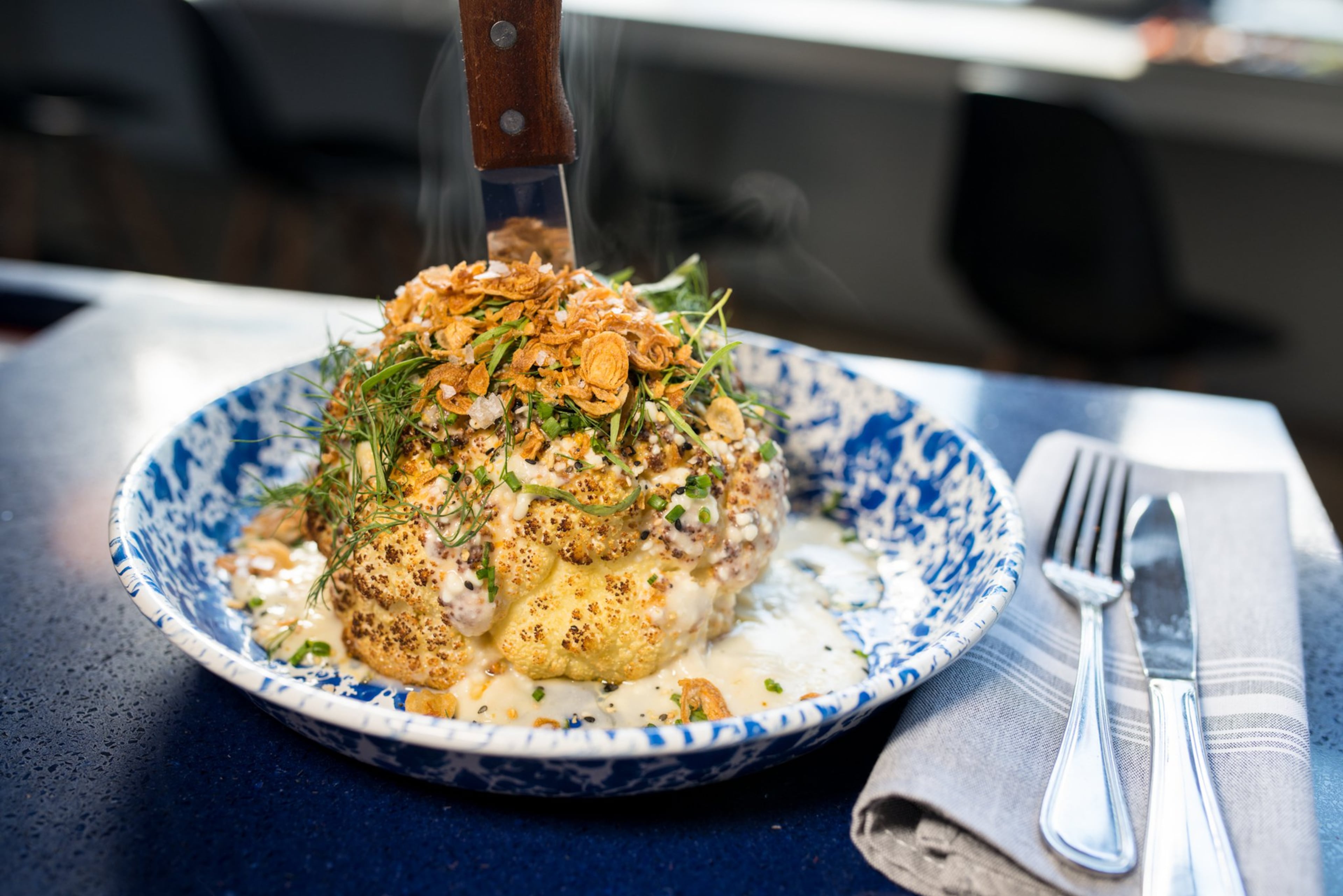 Whiskey Bird Whole Roasted Cauliflower with everything bagel seasoning, smoked Gouda-miso fondue, crispy shallots and herbs. Photo credit- Mia Yakel.