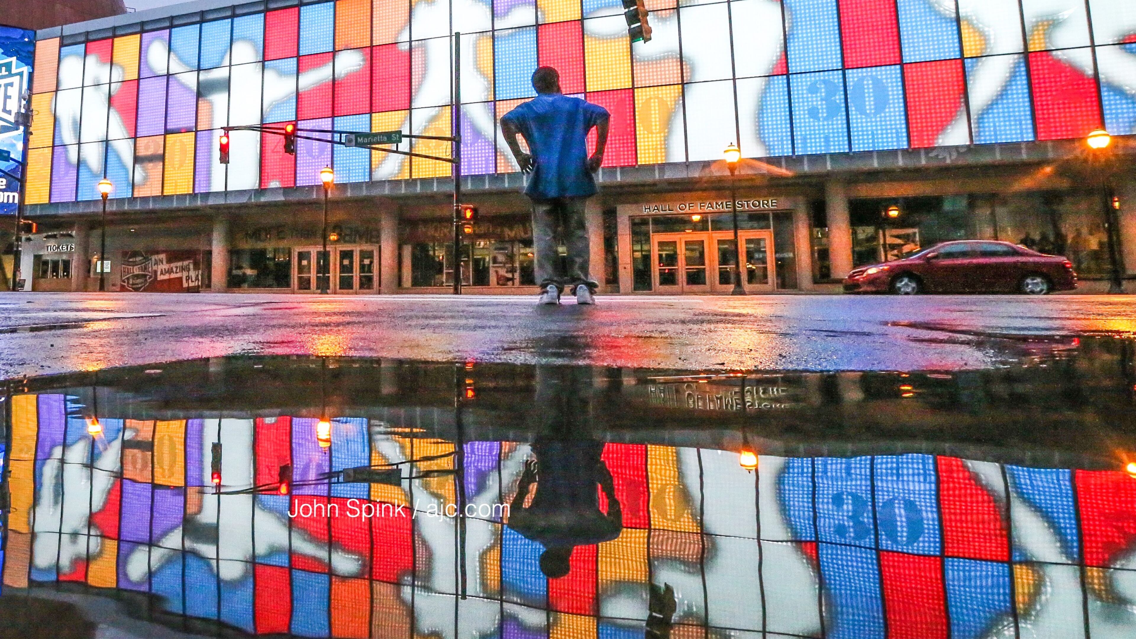 Water from days of rain in metro Atlanta showed a reflection of Kenneth Brown as he crossed in front of the College Football Hall of Fame on Marietta Street early Thursday. JOHN SPINK / JSPINK@AJC.COM