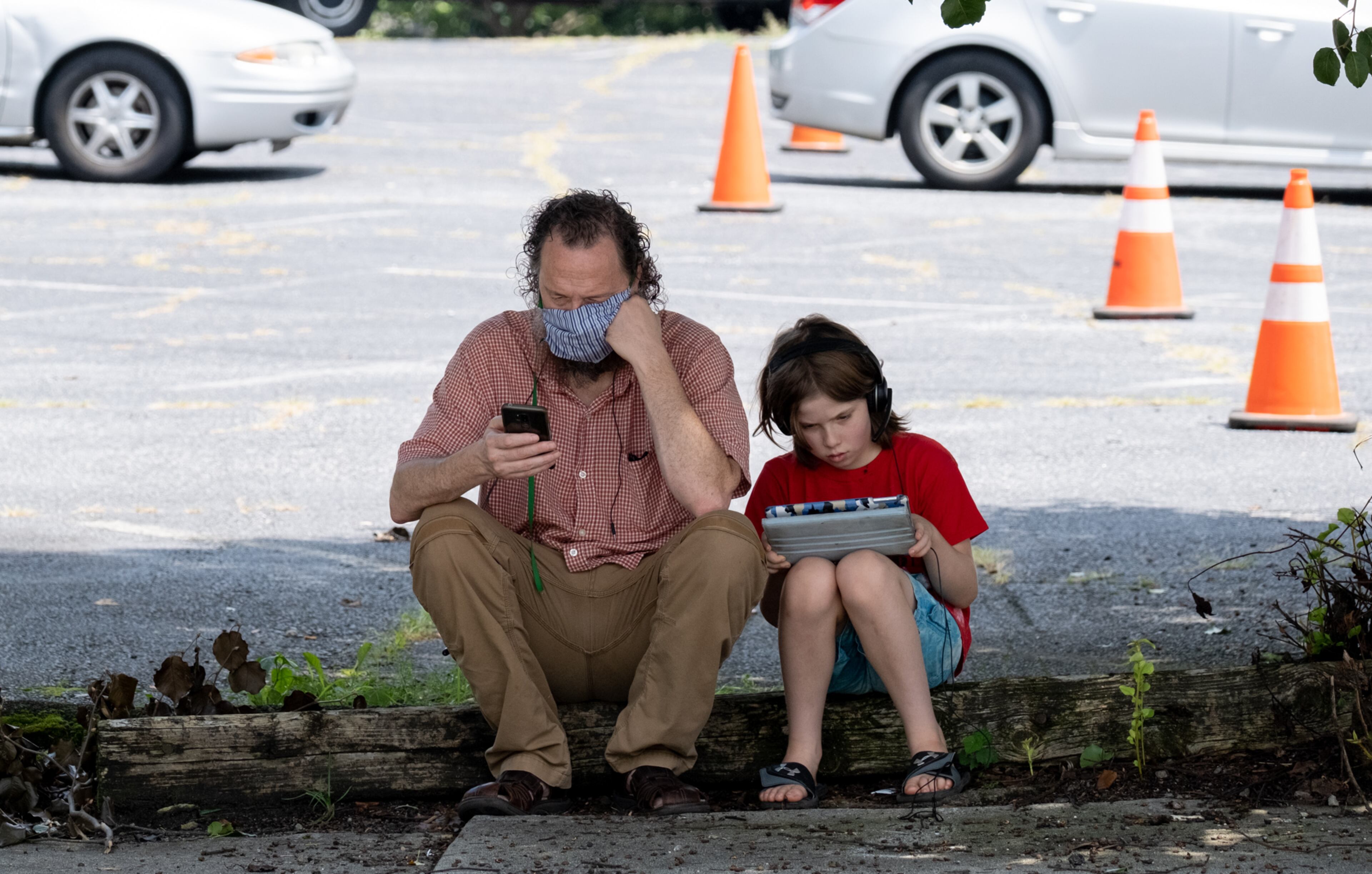 Doug Williams and his son Carter, 8, sit in the shade while waiting to take COVID-19 tests at a CORE testing site at Antioch Baptist Church North in Northwest Atlanta on Thursday, July 16, 2020. The family from East Lake is planning to go visit elderly relatives and wanted to get tested to make sure they could safely visit. They are planning to quarantine until they travel. Ben Gray for the Atlanta Journal-Constitution