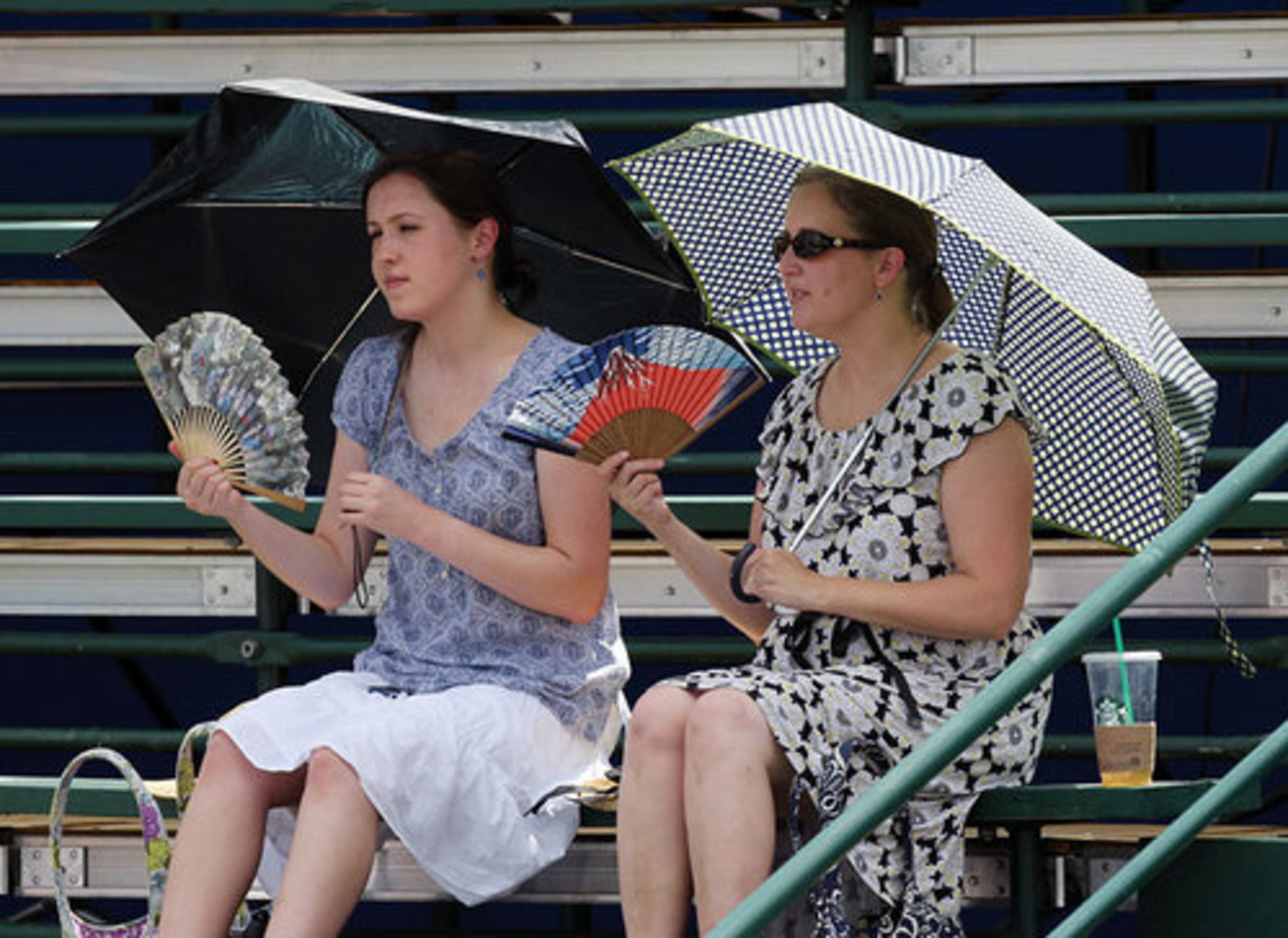 Tennis fans Kristin Doyle (right) with her daughter Frances Doyle, Marietta, use fans and an umbrella while watching play at the Atlanta Open tennis tournament in Atlanta on Monday, July 16, 2012.