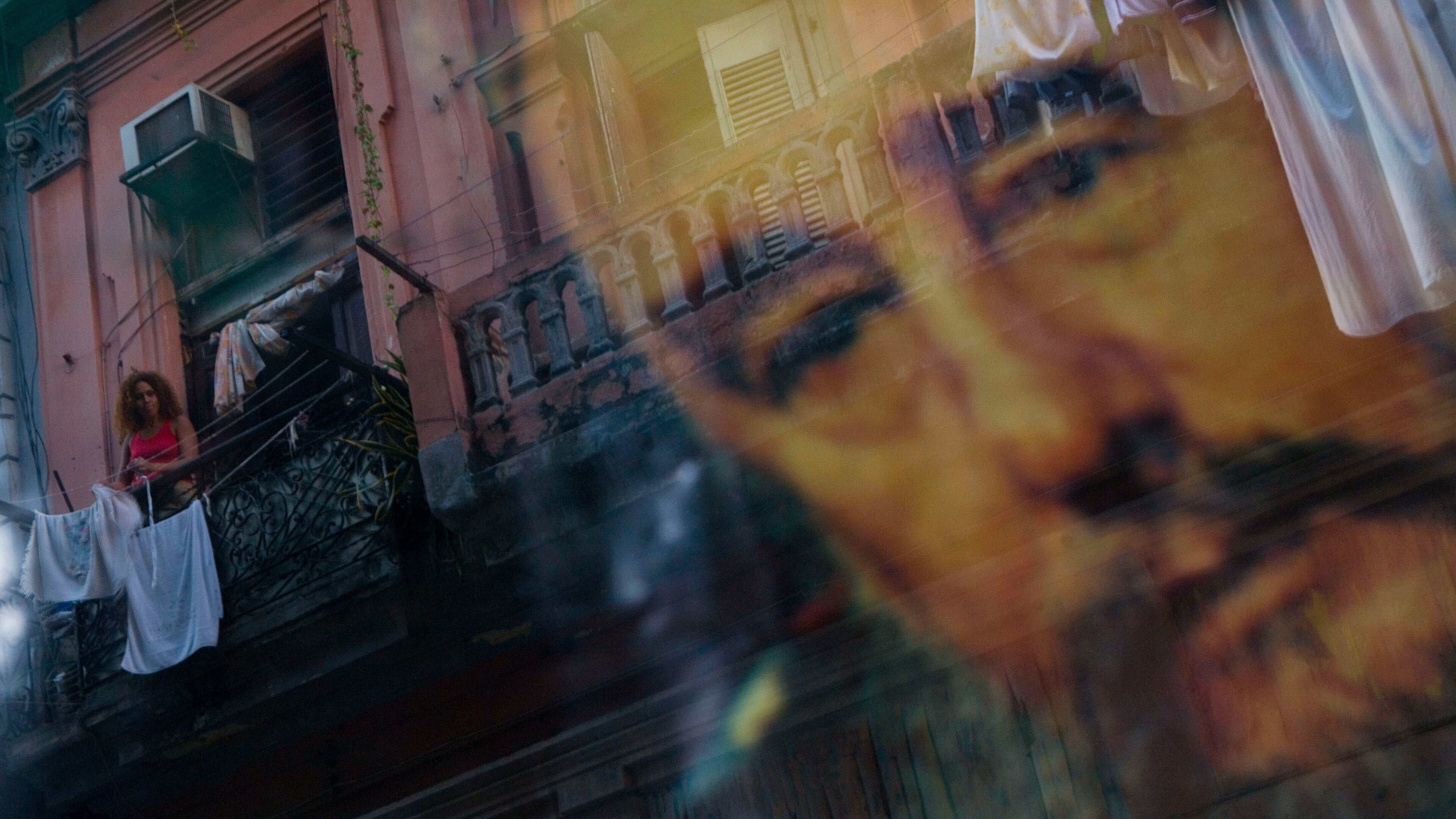 FILE - A Cuban woman hanging laundry on her balcony is seen reflected in a glass window decorated with a poster of Cuba's leader Fidel Castro in Old Havana, Cuba, Thursday, Dec. 27, 2007. (AP Photo/Dado Galdieri, File)