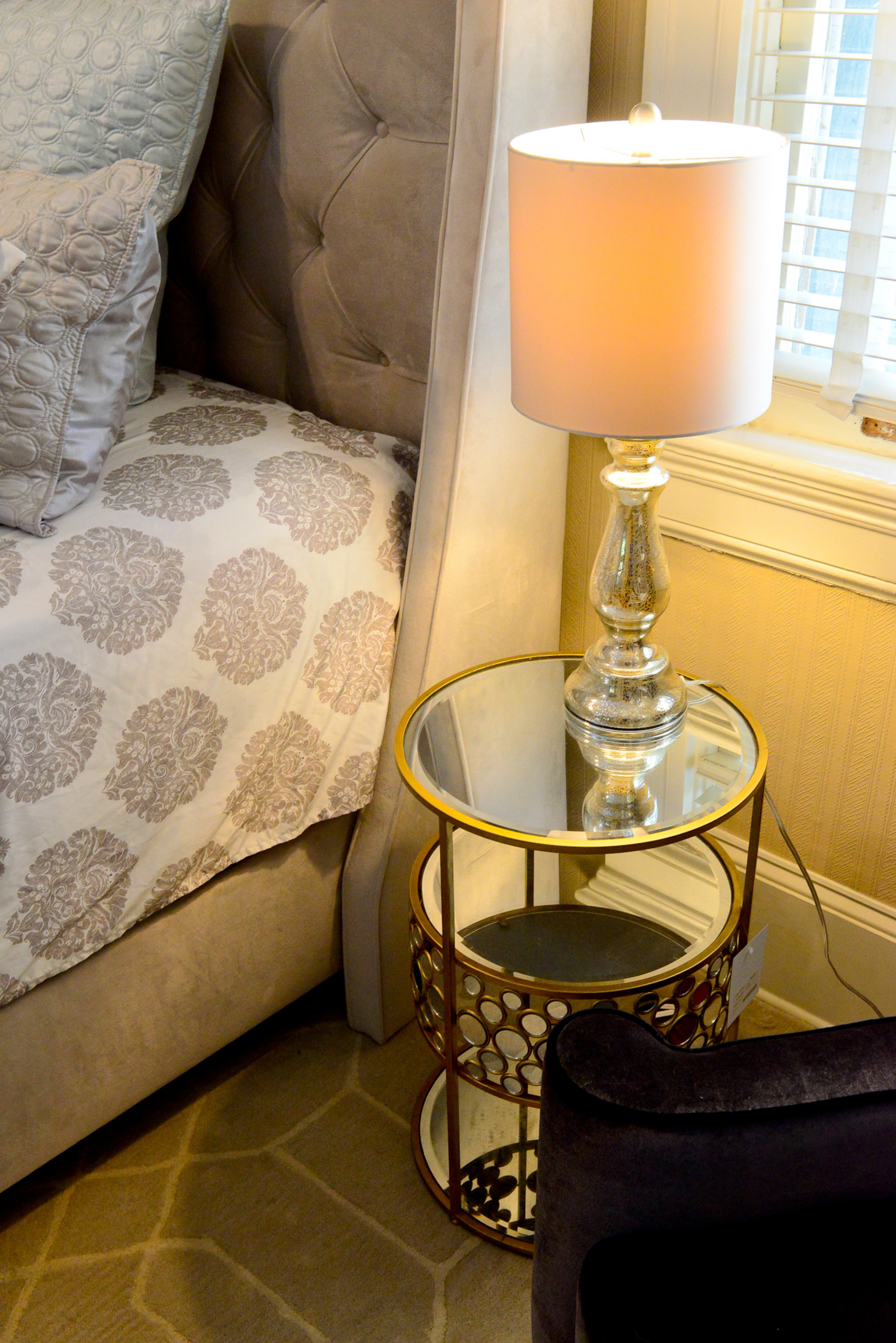 A small, round mirrored end table, from Westside Foundry, is nestled in between the One Kings Lane bed and a Joss & Main armchair.