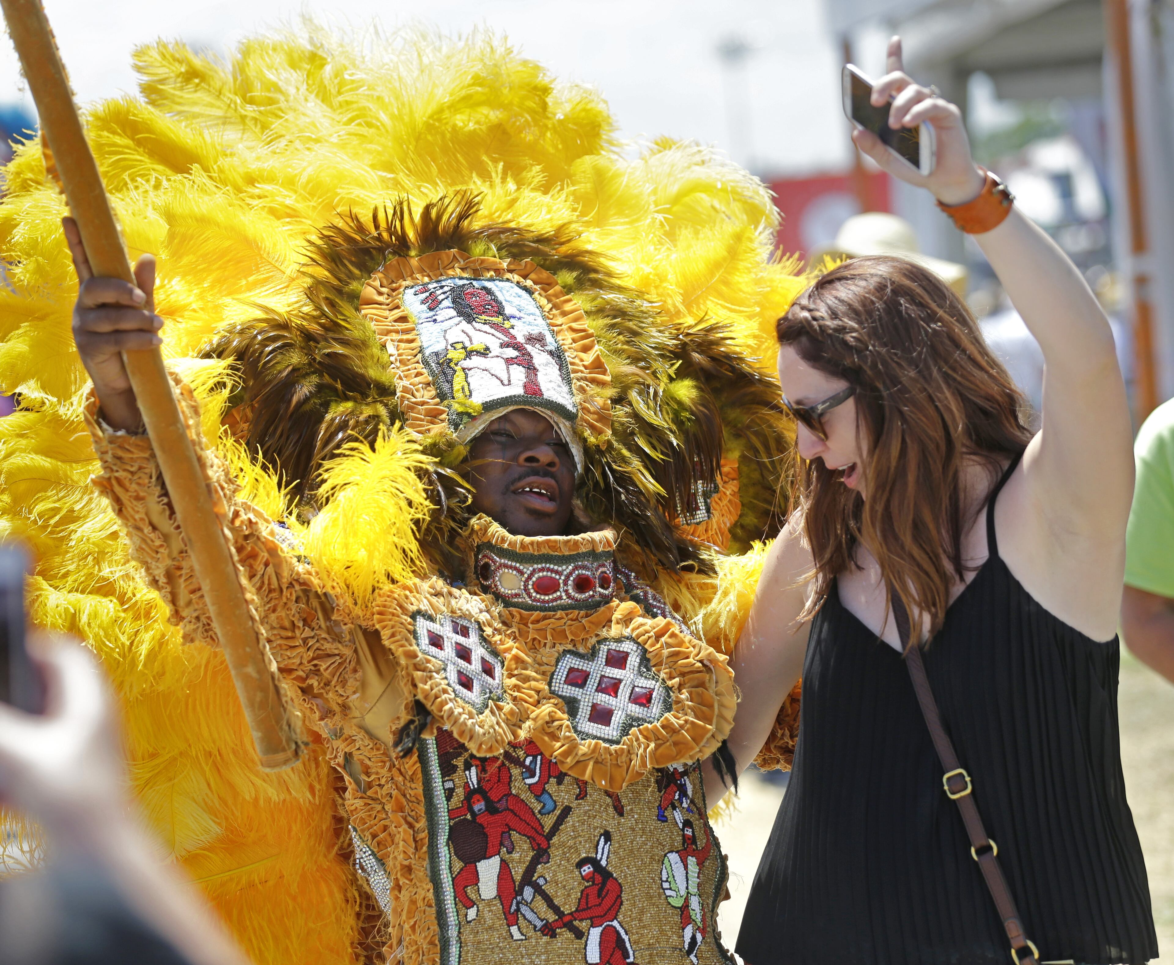 A member of the New Orleans Mardi Gras Indian Rhythm Section, with the Algiers Warriors and Golden Comanche Mardi Gras Indians, dances with a festival-goer in a second line parade at the New Orleans Jazz and Heritage Festival in New Orleans, Friday, May 1, 2015. (AP Photo/Gerald Herbert)