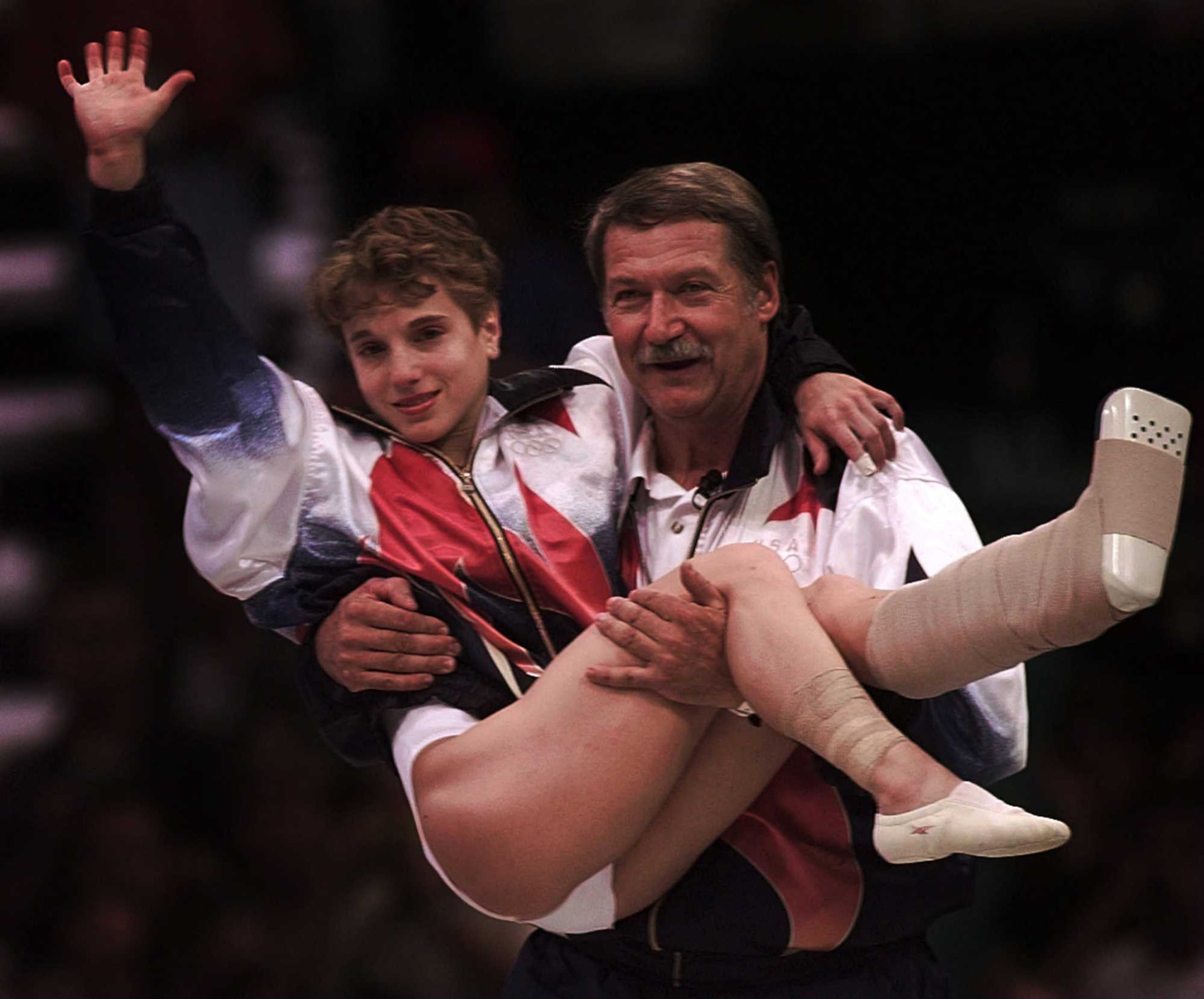 U.S. gymnastics coach Bela Karolyi carries an injured Kerri Strug to the medal ceremony after her vault helped the American women win the gold medal at the 1996 Olympics in Atlanta. AJC file photo