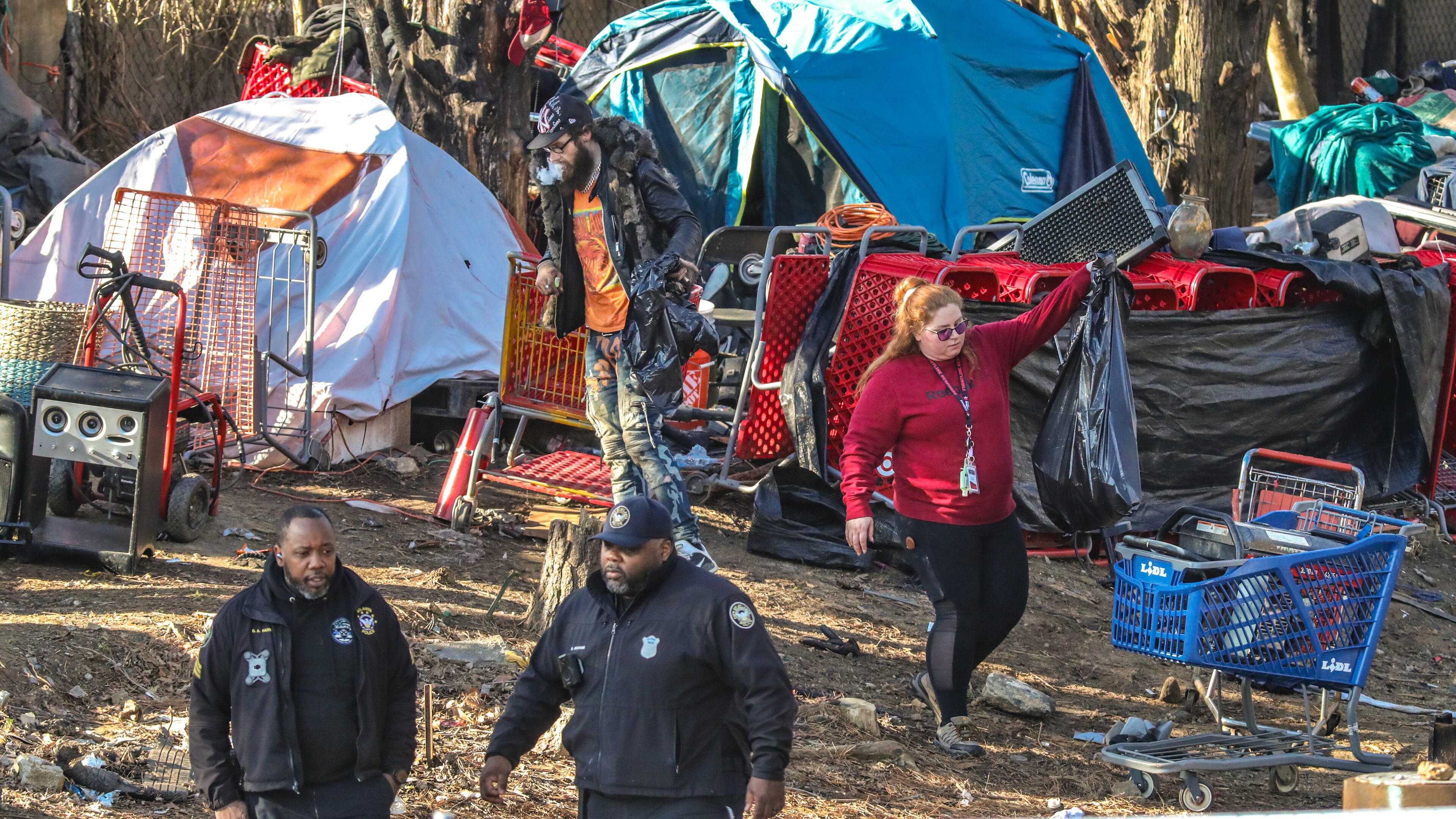 A member of the cleanup crew (right) helps a homeless man (left) gather his things. The city of Atlanta began a major new effort to clear out homeless people living under bridges, and encampments on Monday, Feb. 26, 2024. Georgia DOT employees began cleaning up and area supervised by a half dozen Atlanta police officers located in the 2600 block of Buford Hwy just north of Lenox Road in Atlanta where an encampment exists in an wooded area. The city has declined to share most details of the operation publicly, including which specific bridge areas will be targeted, how many people it anticipates moving, and what kind of housing and locations it might provide to those displaced. (John Spink / John.Spink@ajc.com)