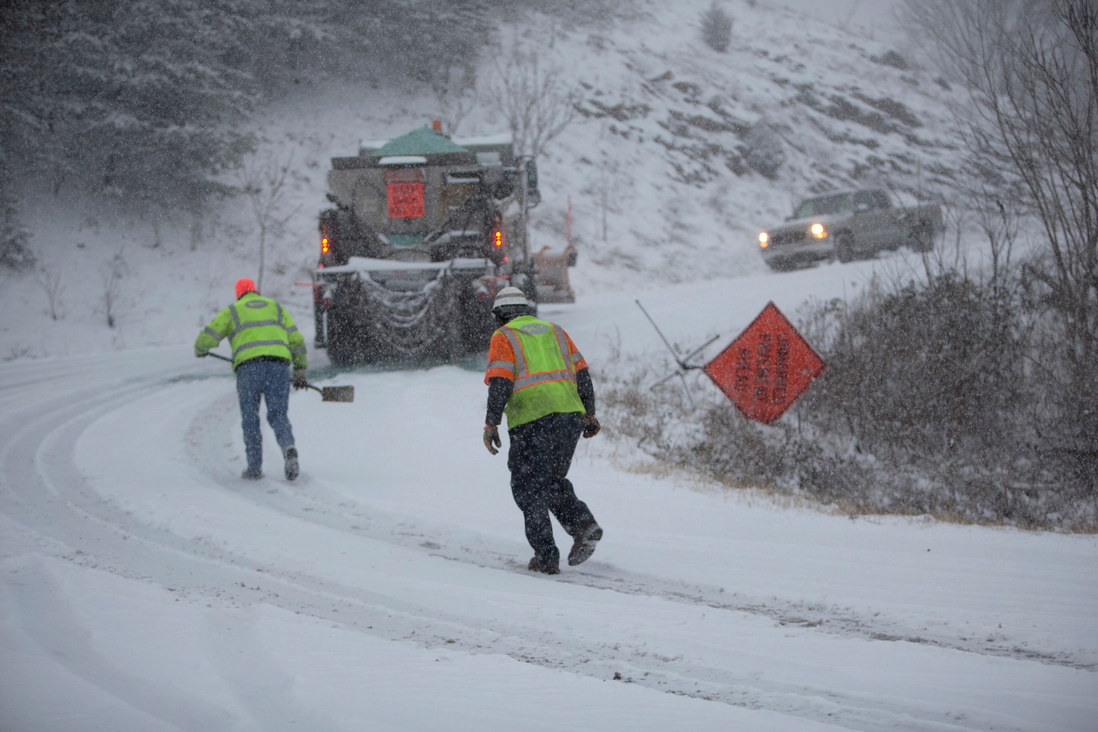 A Virginia Department of Transportation worker brings another VDOT worker a shovel to aide in getting out of a snowy curve on Yellow Mountain Road off of US220-S in Roanoke, Va., Sunday, Dec. 9, 2018. (Stephanie Klein-Davis/The Roanoke Times via AP)