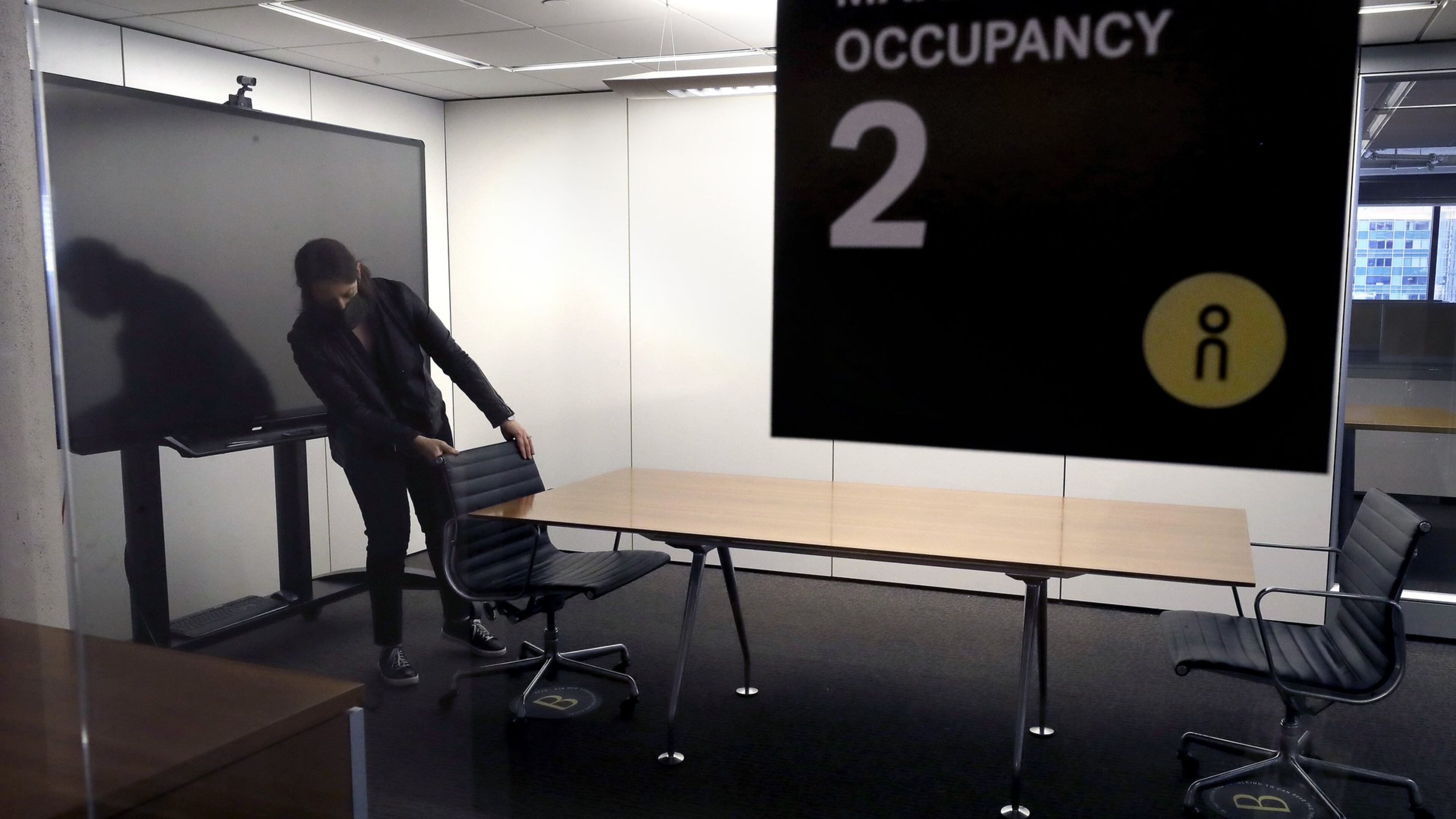 In this Thursday, May 7, 2020 photo, Vice President Rachel Zsembery at the design firm Bergmeyer, positions chairs in a conference room with a designated maximum occupancy of two people, at the firm’s offices, in Boston. Out of concern for the coronavirus Bergmeyer is restructuring the way its workspace is used, including reinstalling dividers on 85 desks at its Boston office that had been removed over the years. (AP Photo/Steven Senne)