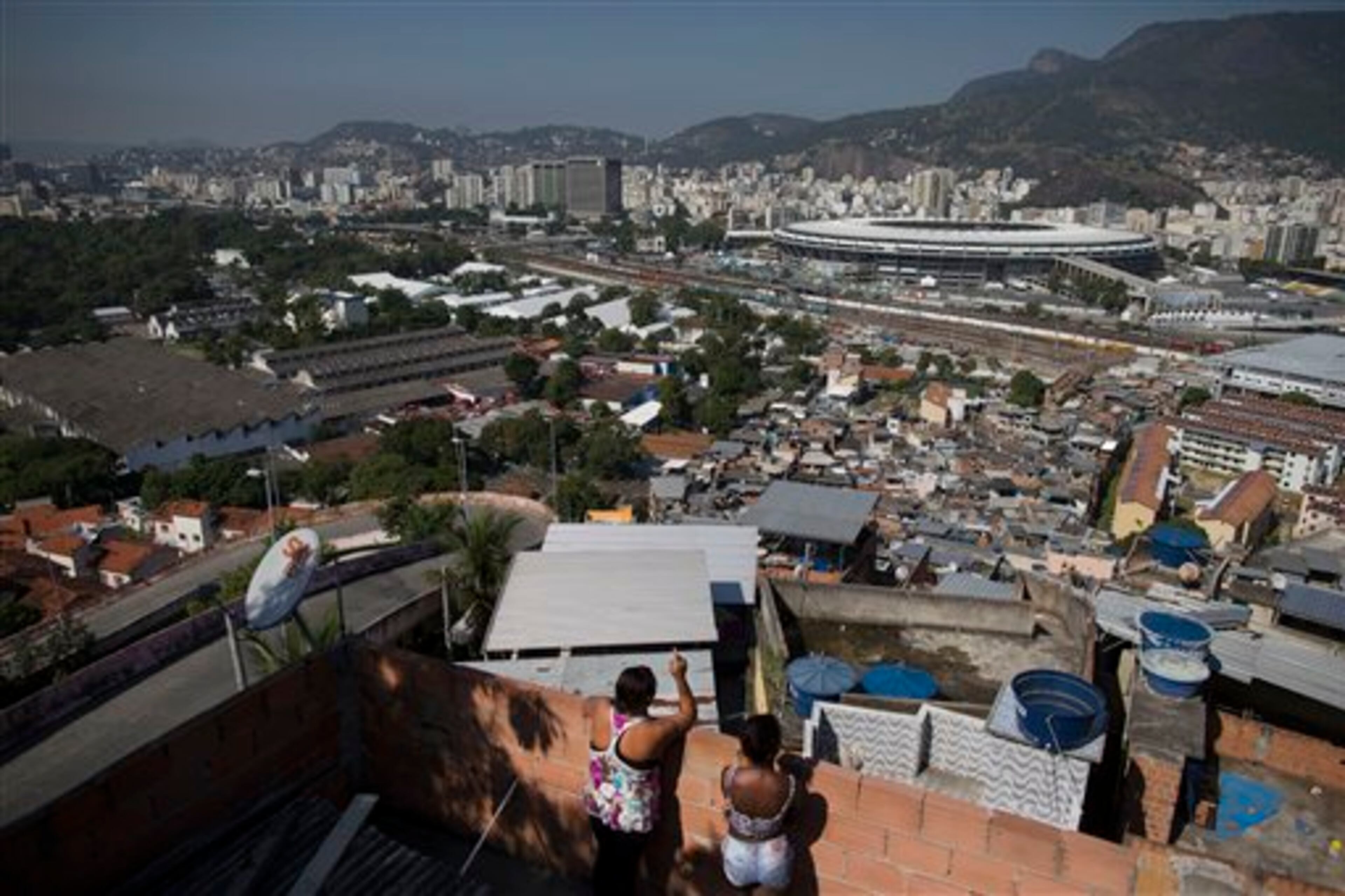 In this Wednesday, June 4, 2014 photo, women visit on a rooftop where they can see Maracana stadium from the Mangueira slum in Rio de Janeiro, Brazil. With tickets to the World Cup tournament expensive and hard to come by, the gulf between Mangueira and Maracana is almost impassable. (AP Photo/Leo Correa)