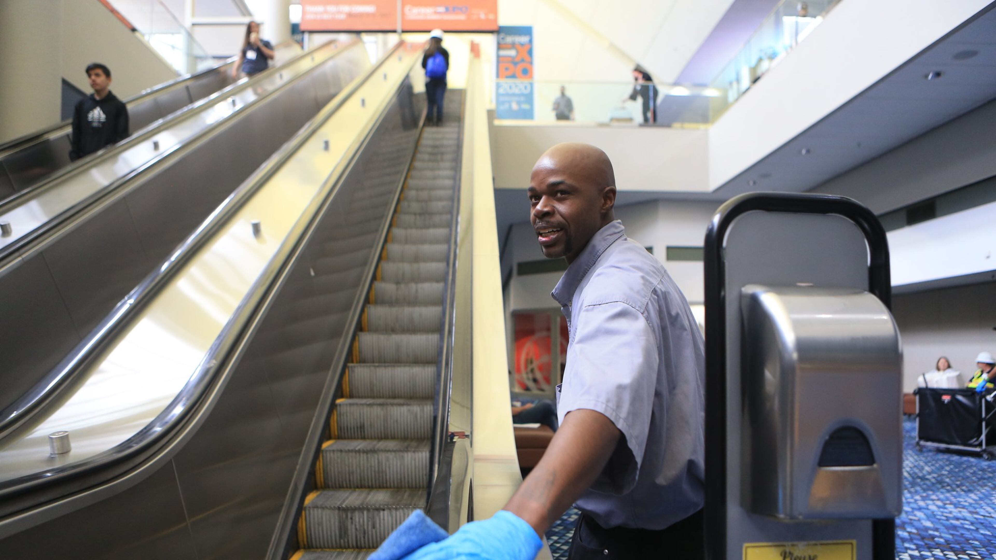 Dion Smith wipes down the escalator during the Construction Education Foundation of Georgia (CEFGA) career expo on Thursday, March 12, 2020, at the World Congress Center in Atlanta. This year, additional safety measures were implemented, including mandatory hard hats and wipe downs of surfaces people touch. CHRISTINA MATACOTTA, FOR THE ATLANTA JOURNAL-CONSTITUTION