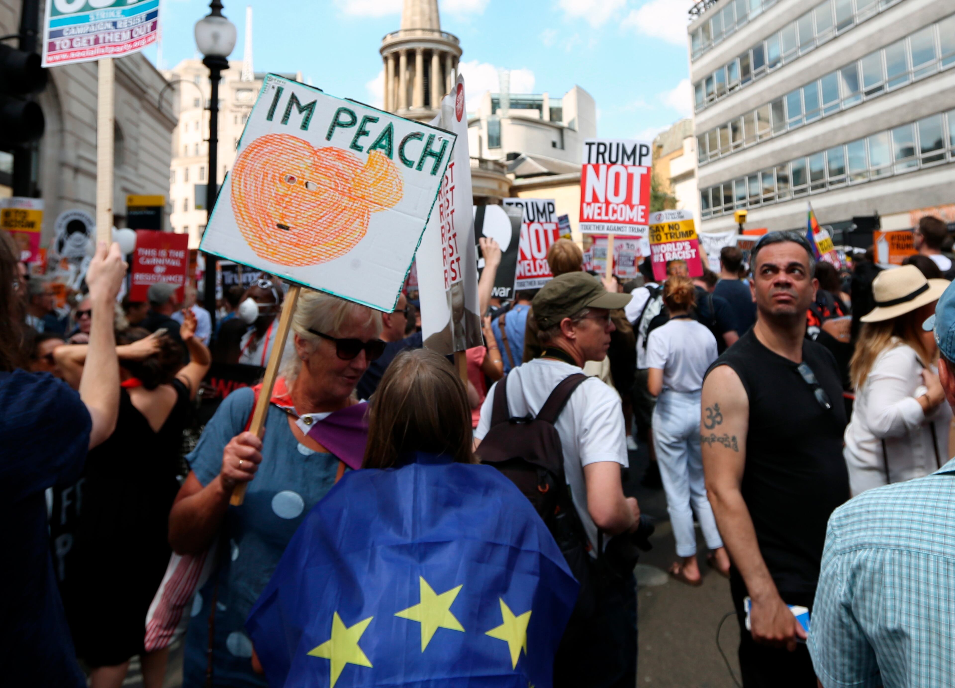 Protestors hold banners during a march opposed to the visit of U.S. President Donald Trump in London, Friday, July 13, 2018. Trump's pomp-filled welcome to Britain was overshadowed Friday by an explosive interview in which he blasted Prime Minister Theresa May, blamed London's mayor for terror attacks against the city and argued that Europe was "losing its culture" because of immigration. (AP Photo/Robert Stevens)