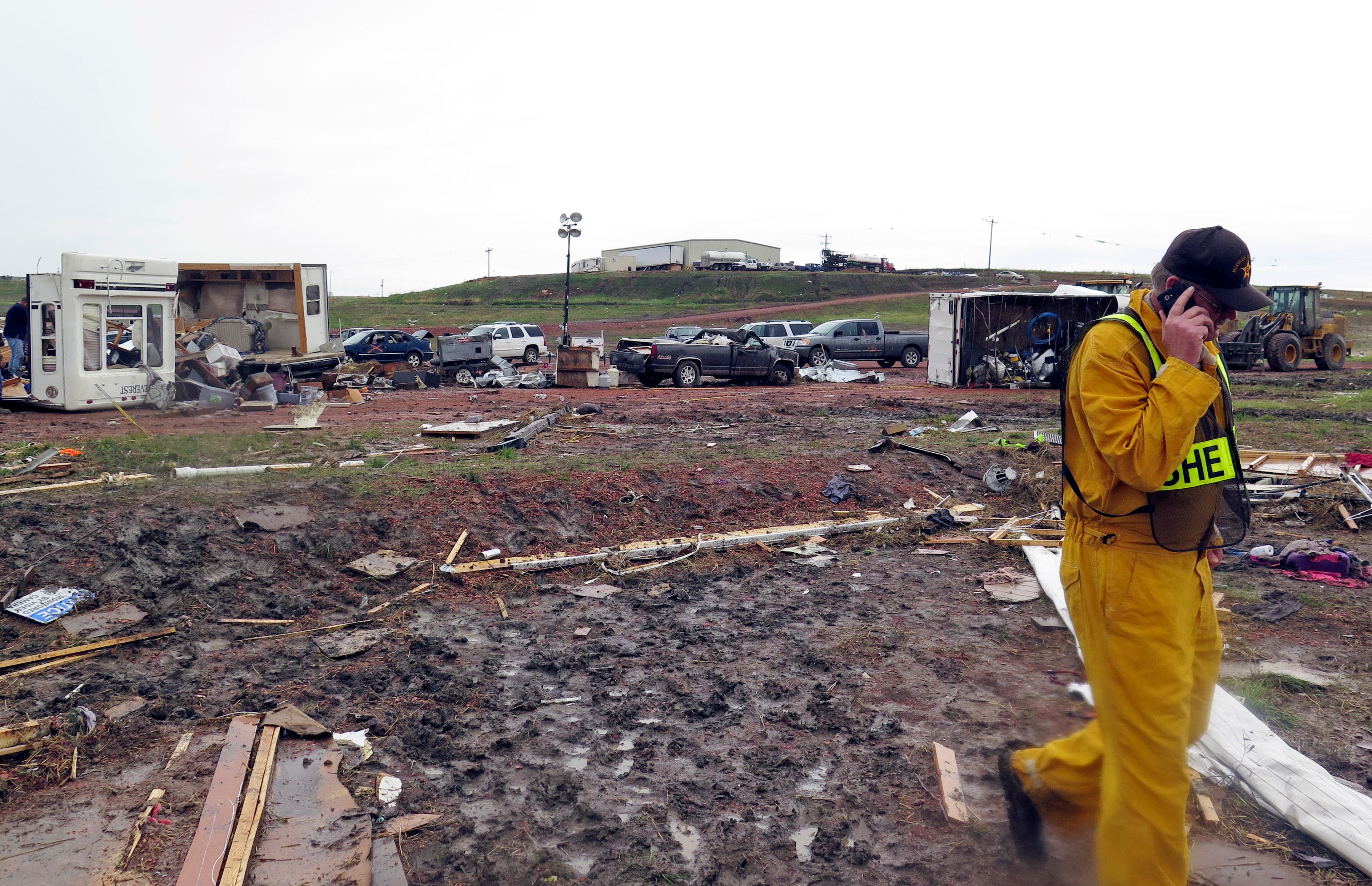 A McKenzie County Sheriff talks on a phone among scatterd debris Tuesday morning, May 27, 2014, after a tornado in Watford City, N.D. Authorities say at least eight trailers were destroyed Monday evening when the twister tore through a camp where oil field workers stay. Nine people were injured, including a 15-year-old girl critically. (AP Photo/Josh Wood)