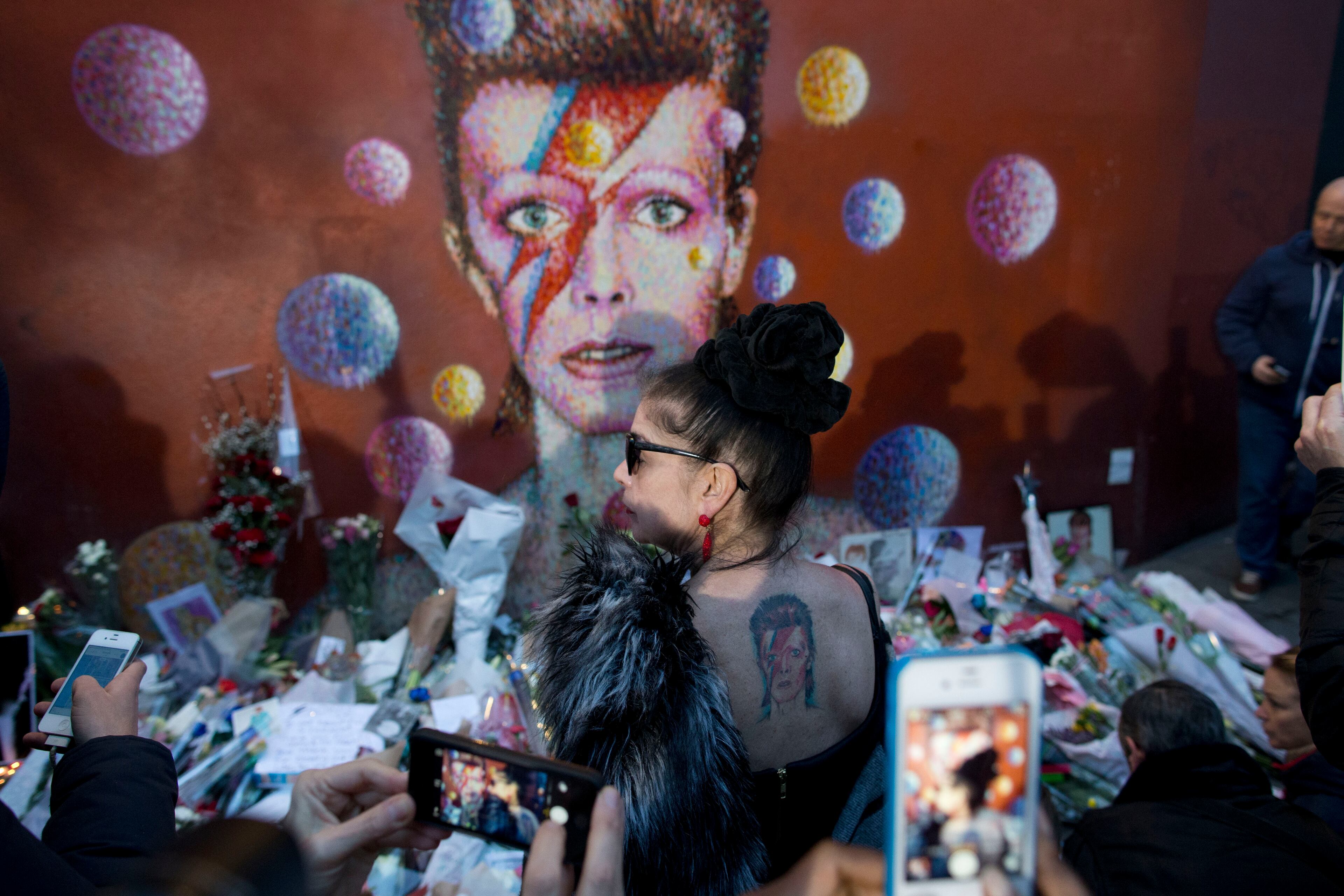 A woman with a tattoo on her back looks at a mural of British singer David Bowie by artist Jimmy C in Brixton, south London, Monday, Jan. 11, 2016. Bowie, the other-worldly musician who broke pop and rock boundaries with his creative musicianship, nonconformity, striking visuals and a genre-spanning persona he christened Ziggy Stardust, died of cancer Sunday aged 69. He was born in Brixton. (AP Photo/Matt Dunham)