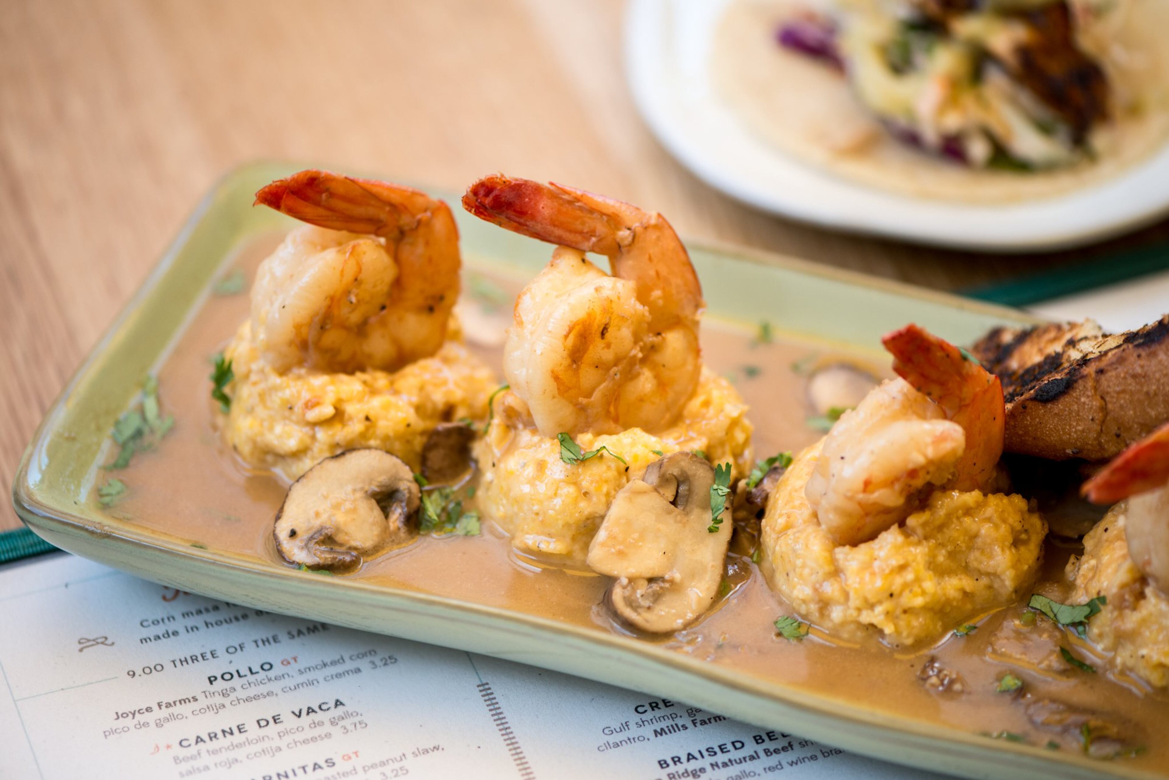 Creole Shrimp and Grits with gulf shrimp, garlic, herb creole sauce, mushrooms, cilantro, Mills Farms grits, and grilled country bread. Photo credit- Mia Yakel.