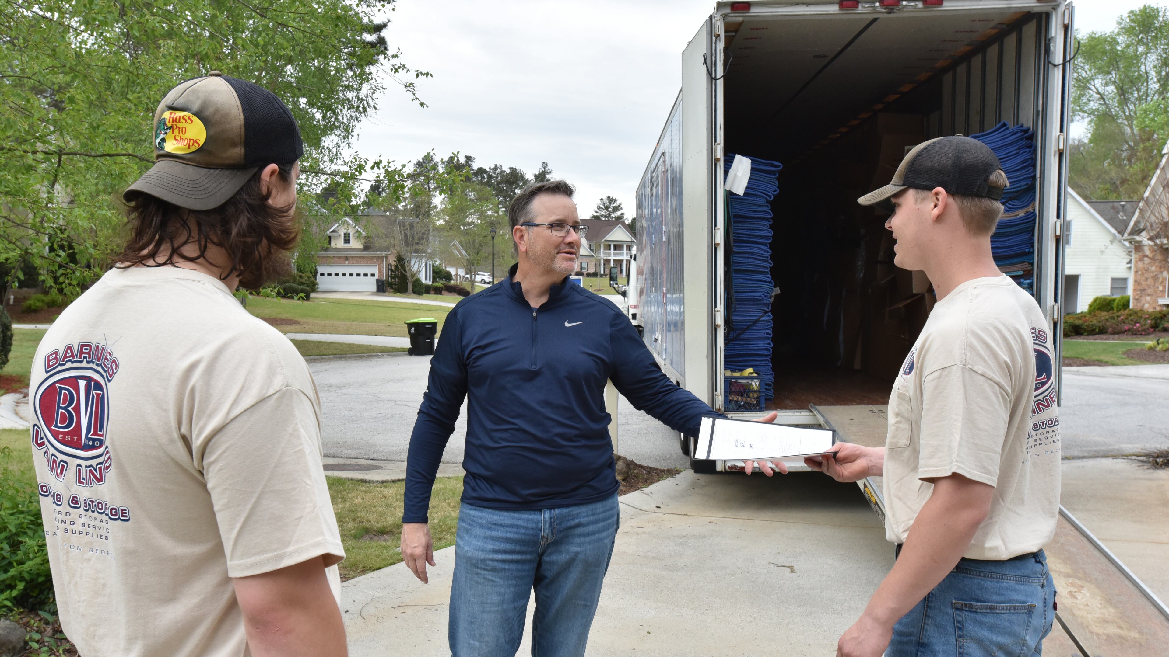 Chris New (center), owner of Barnes Van Lines, hands over paperwork to Anson Strickland as Joe Nowak (left) looks on while moving a family in Villa Rica on Thursday, April 15, 2021. (Hyosub Shin / Hyosub.Shin@ajc.com)