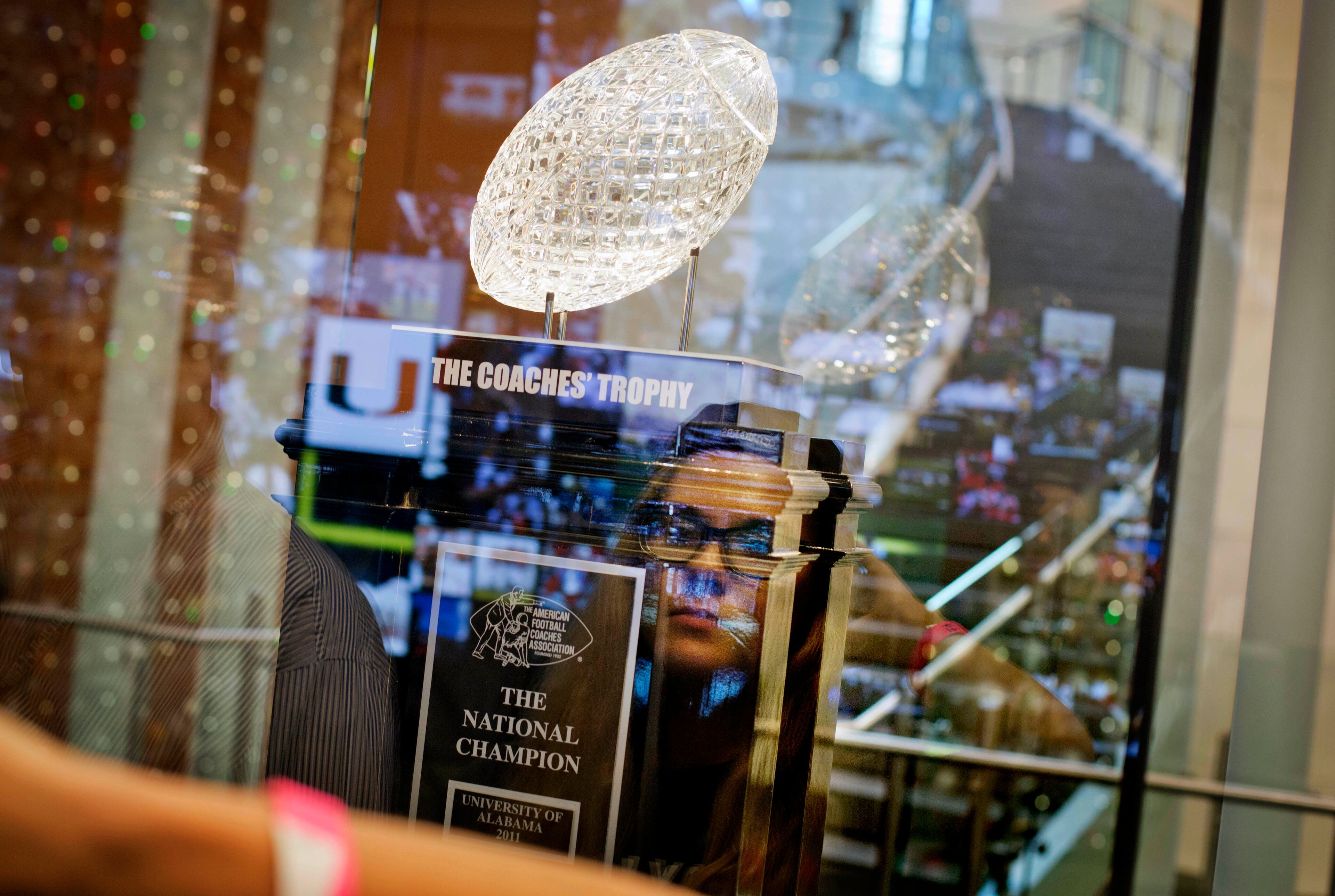 Callie Farley, 17,of Suwannee, Ga, is reflected in glass while looking at the Coaches' Trophy on display during a tour at the College Football Hall of Fame, Wednesday, Aug. 13, 2014, in Atlanta. One hundred contest winners who wrote an essay detailing their love of college football were selected to stay with a guest overnight in Atlanta's College Football Hall of Fame before its grand opening and win a year's supply of Chick-fil-A. The crowd of 200 who came from as far away as Hawaii were among the first to experience the College Football Hall of Fame and Chick-fil-A Fan experience before it opens to the public on Aug. 23. After touring the exhibits guest were served dinner on the football field before pitching their tents on the turf and settling in for the night as college football themed movies such as "Rudy" were played on the jumbotron. The hall was previously located in South Bend, Indiana, but was plagued by poor attendance. (AP Photo/David Goldman) (AP Photo/David Goldman)