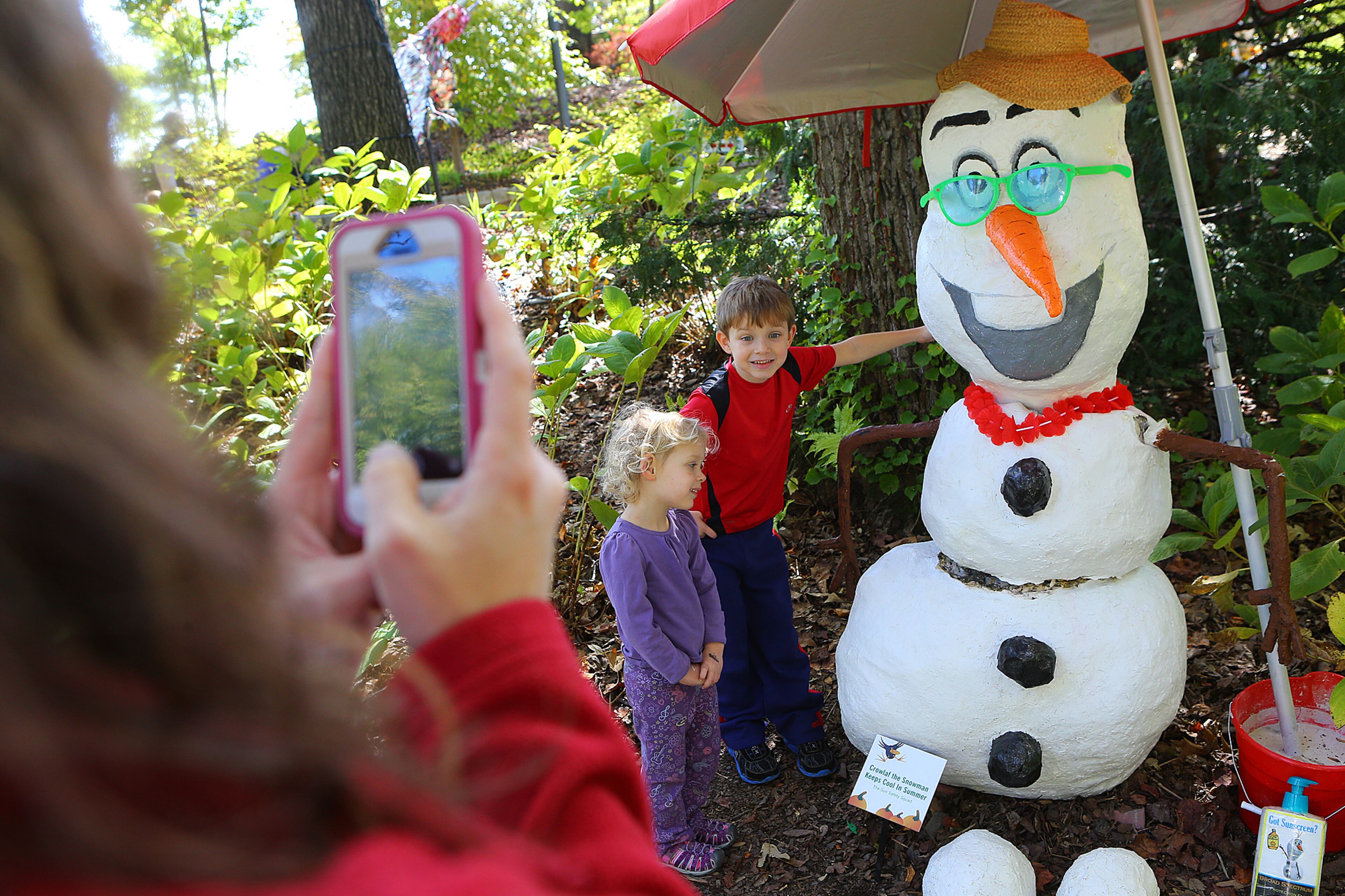 Vicki Cheplak, Marietta, snaps a picture of her children Nathan, 7, and Lyla, 3, with Crowlaf the Snowman Keeps Cool in Summer, one of about 100 scarecrows during Goblins in the Garden. CURTIS COMPTON / CCOMPTON@AJC.COM