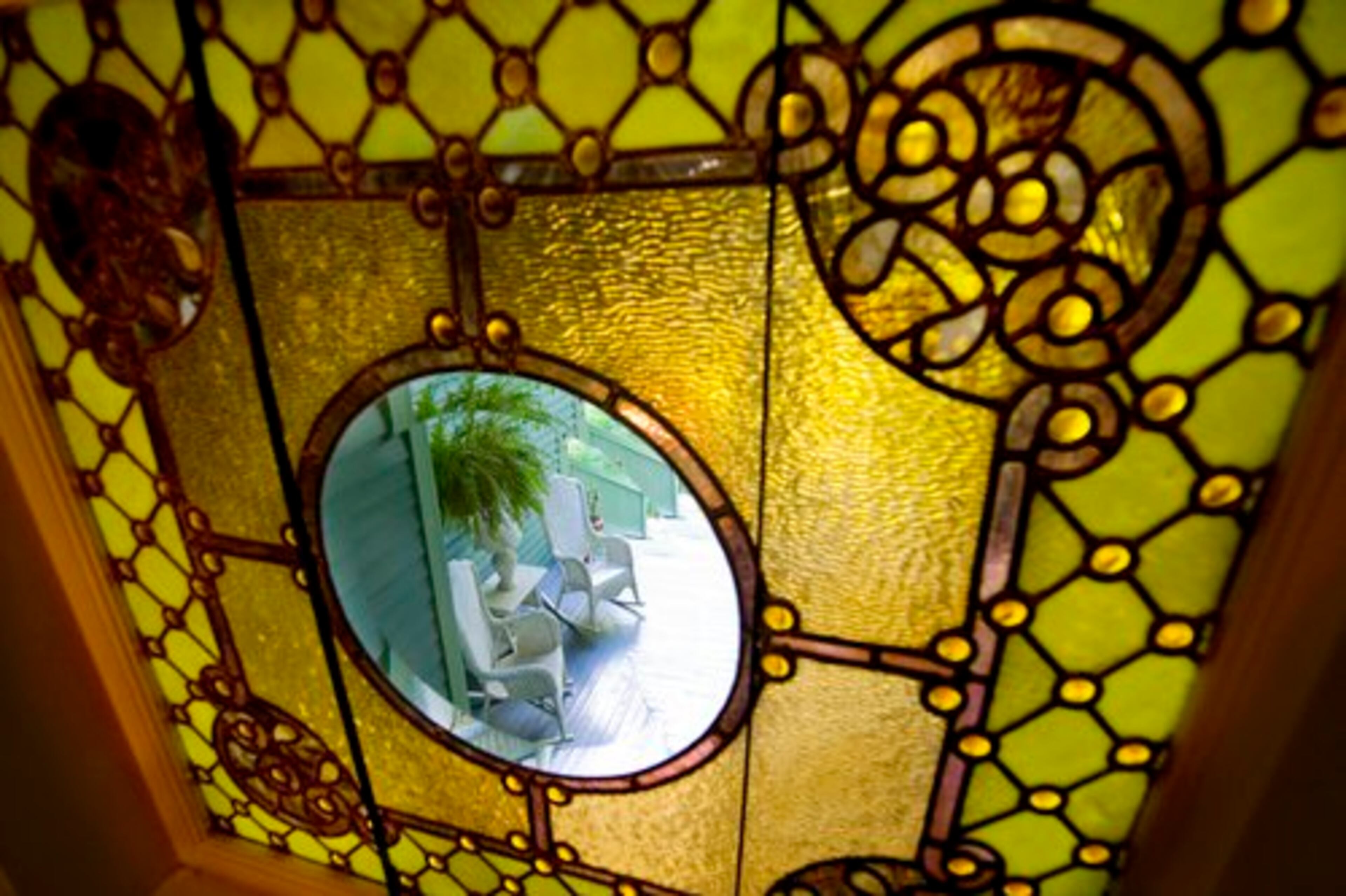 A view of the back porch through a detail of a larger, two-story, five-panel stained glass window.