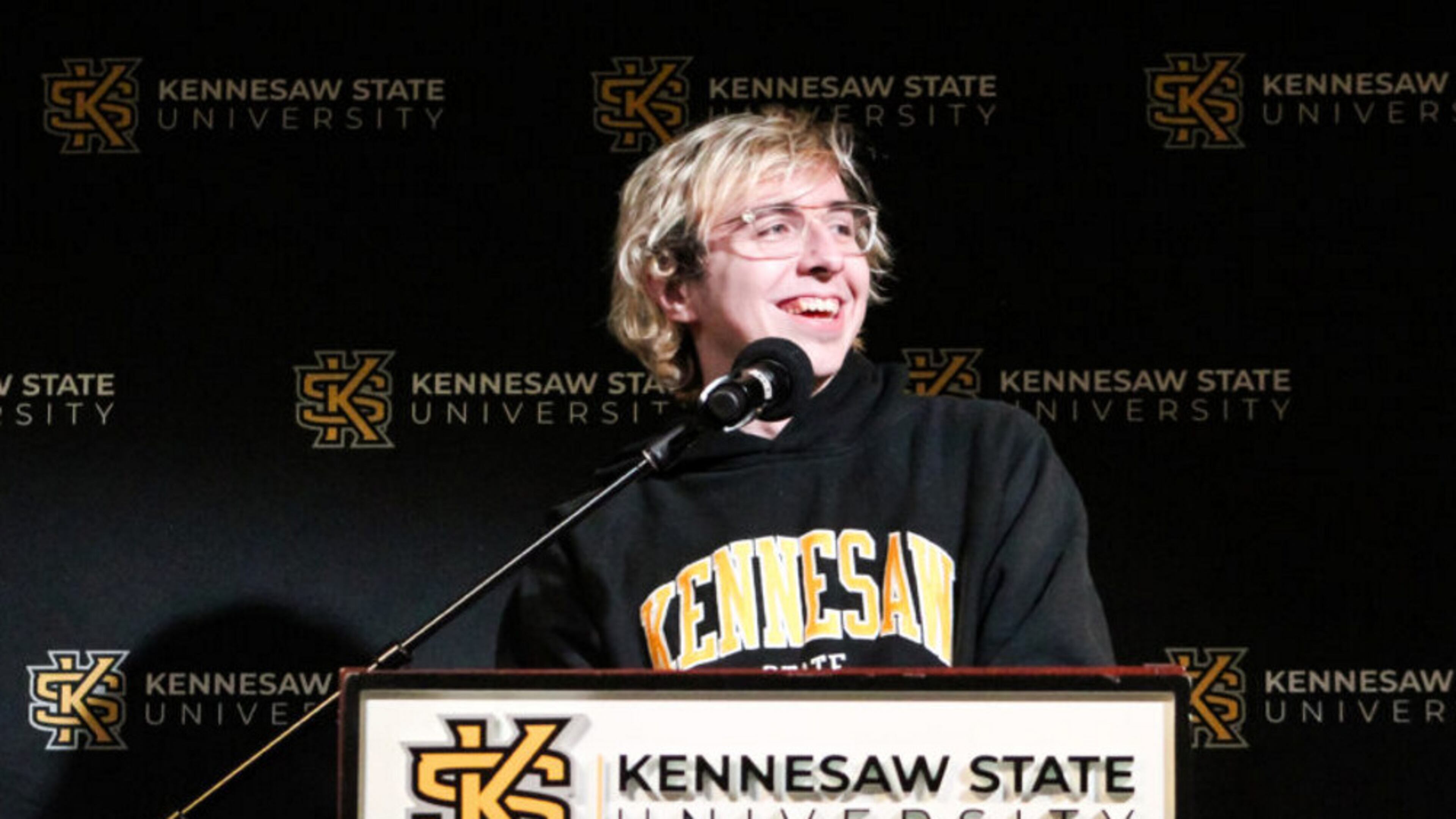 KSU alumnus Raymond Goslow on his “Jeopardy!”: Blonde, white man speaking at podium with KSU BANNER