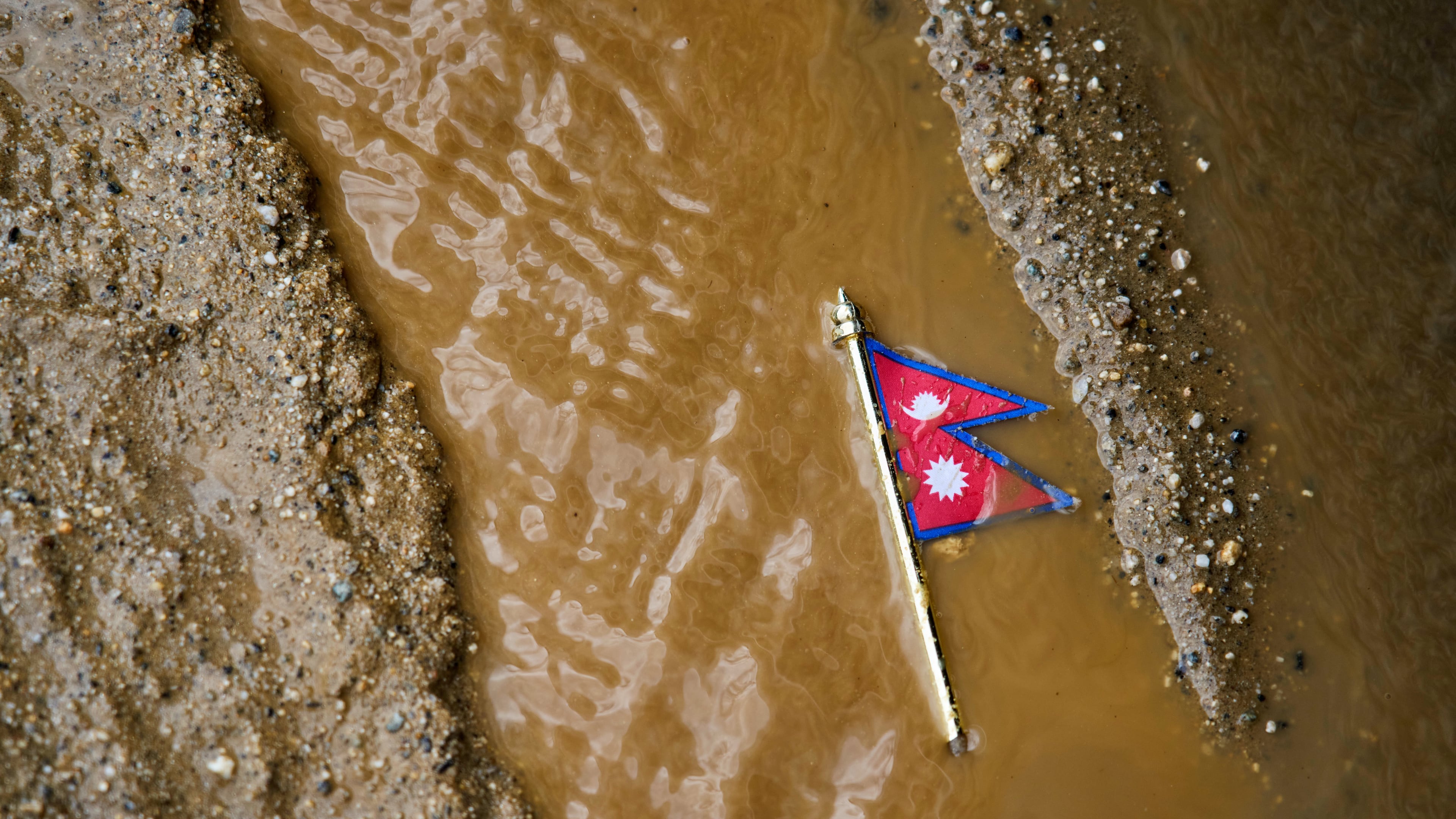 A Nepal flag lies on a muddy track near the banks of the Trishuli river in Dhading District, Nepal, Sunday, Aug. 30, 2026. (AP Photo/Niranjan Shrestha)