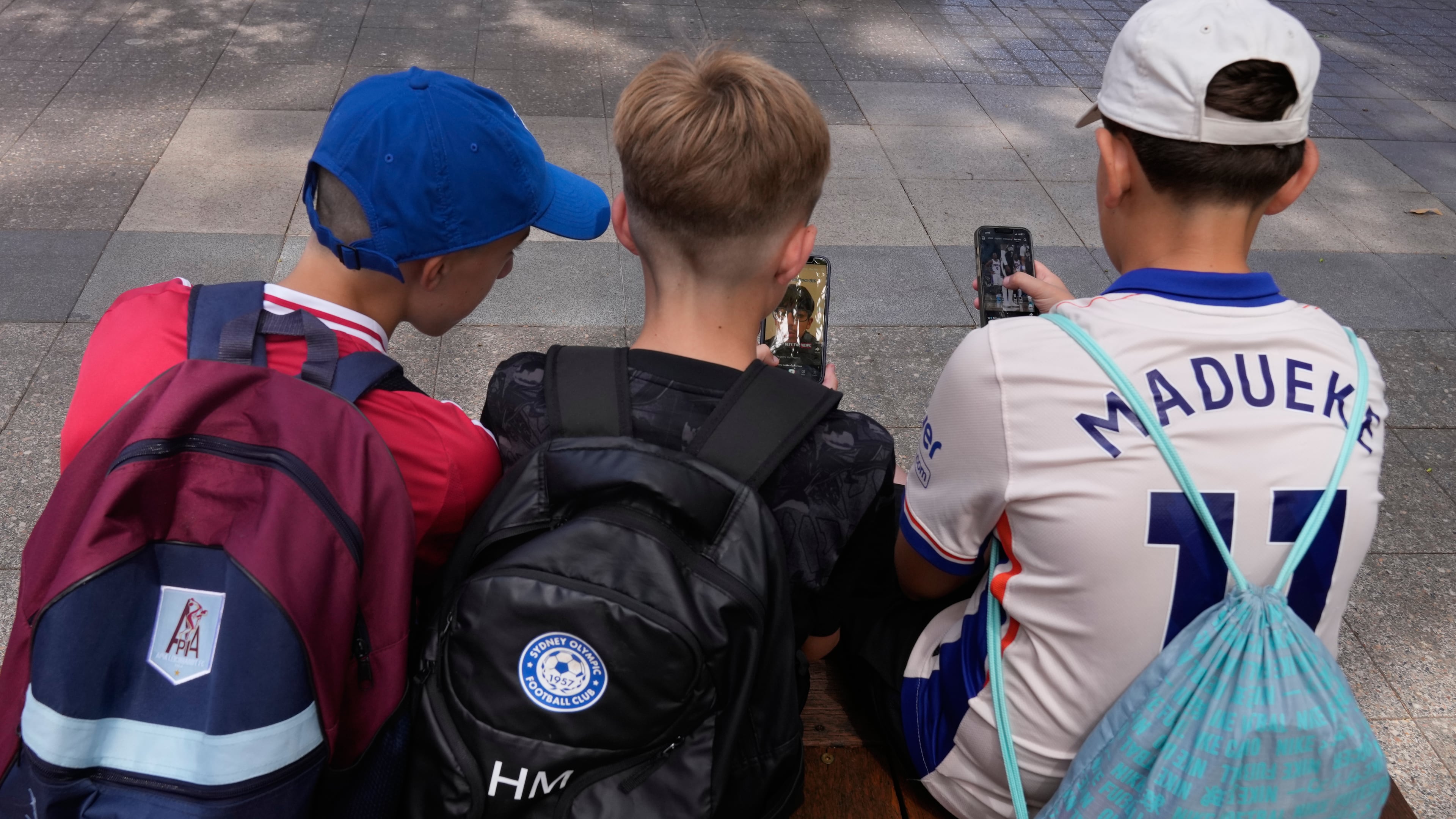 FILE - Three boys use their phones while sitting outside a school in Sydney, Monday, Dec. 8, 2025. (AP Photo/Rick Rycroft, File)
