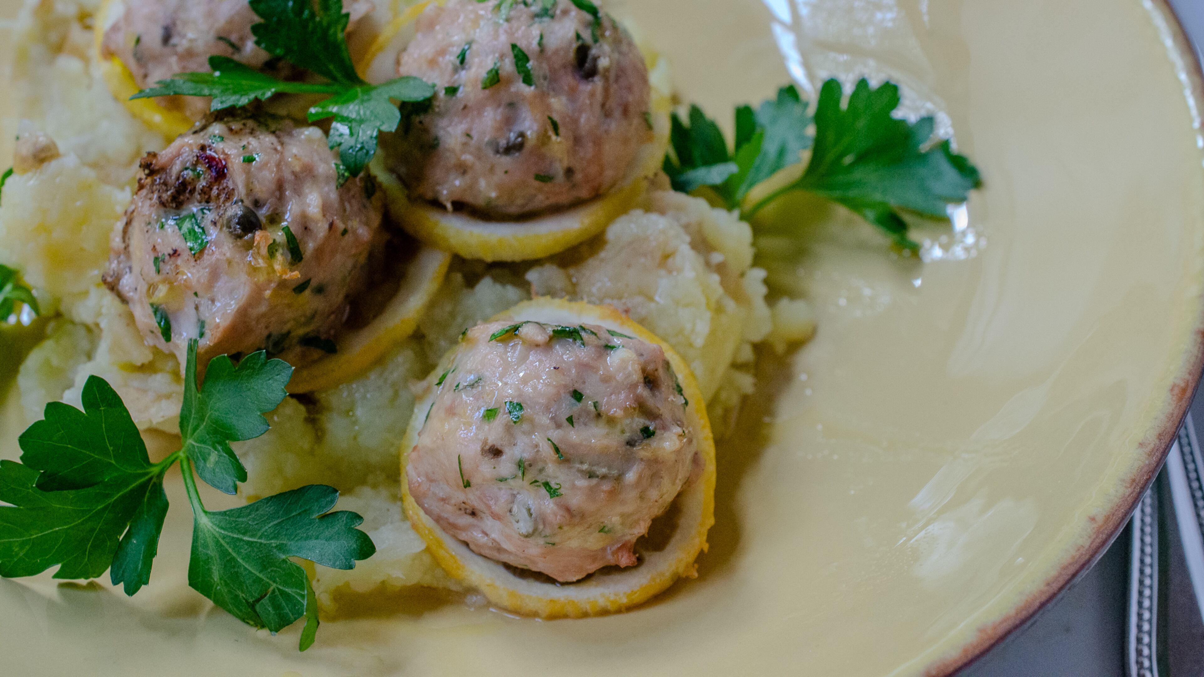 Baked chicken piccata meatballs with sliced lemon, fresh parsley and extra virgin olive oil. (Virginia Willis for The Atlanta Journal-Constitution)
