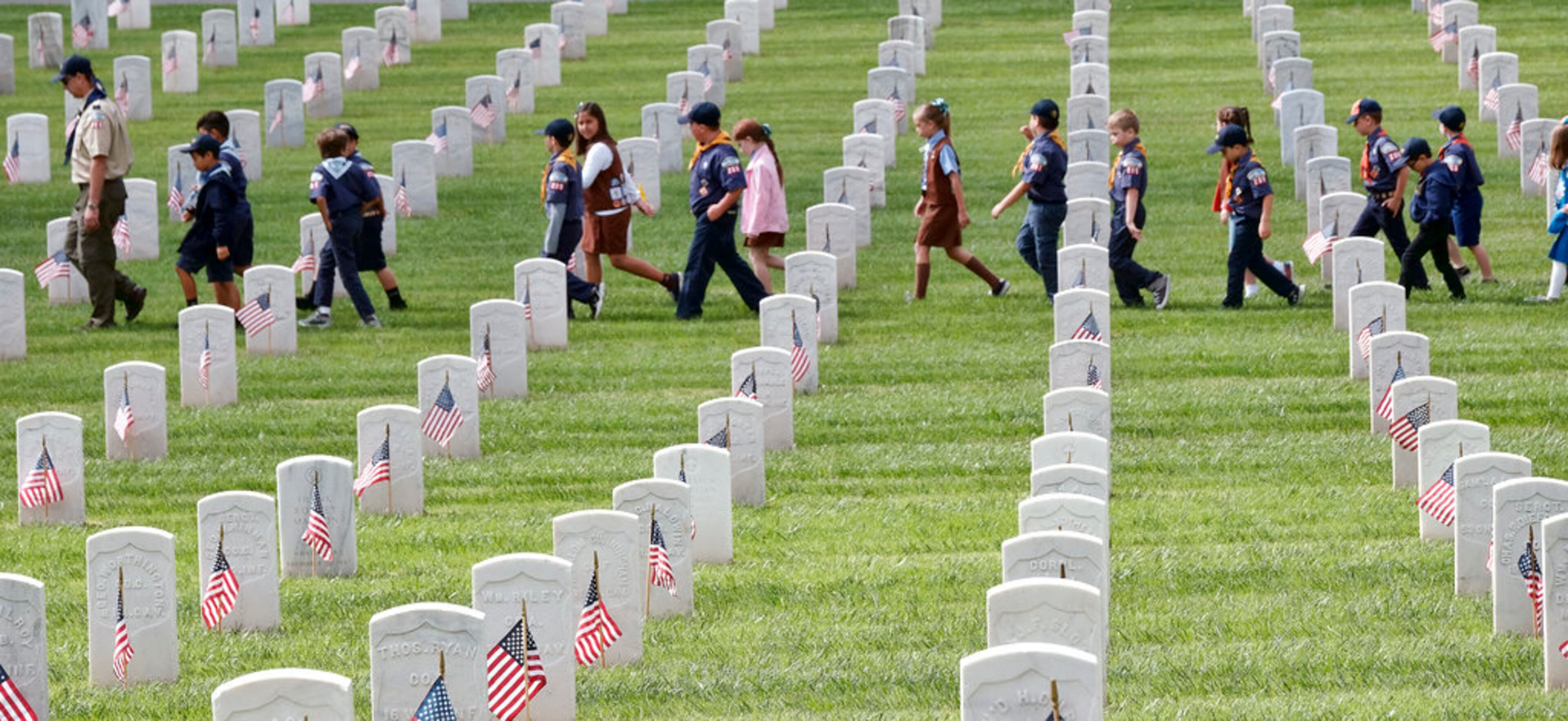 Boy Scouts and Girl Scouts walk between grave stones after helping place flags at the Los Angeles National Cemetery on Saturday, May 26, 2018. Thousands of scouts have placed American flags on the graves of veterans in a ceremony ahead of Memorial Day. More than 6,000 children participated in the event. Each uniformed scout placed a flag in the ground by each grave and saluted. Organizers say nearly 90,000 flags were placed in tribute. (AP Photo/Richard Vogel)