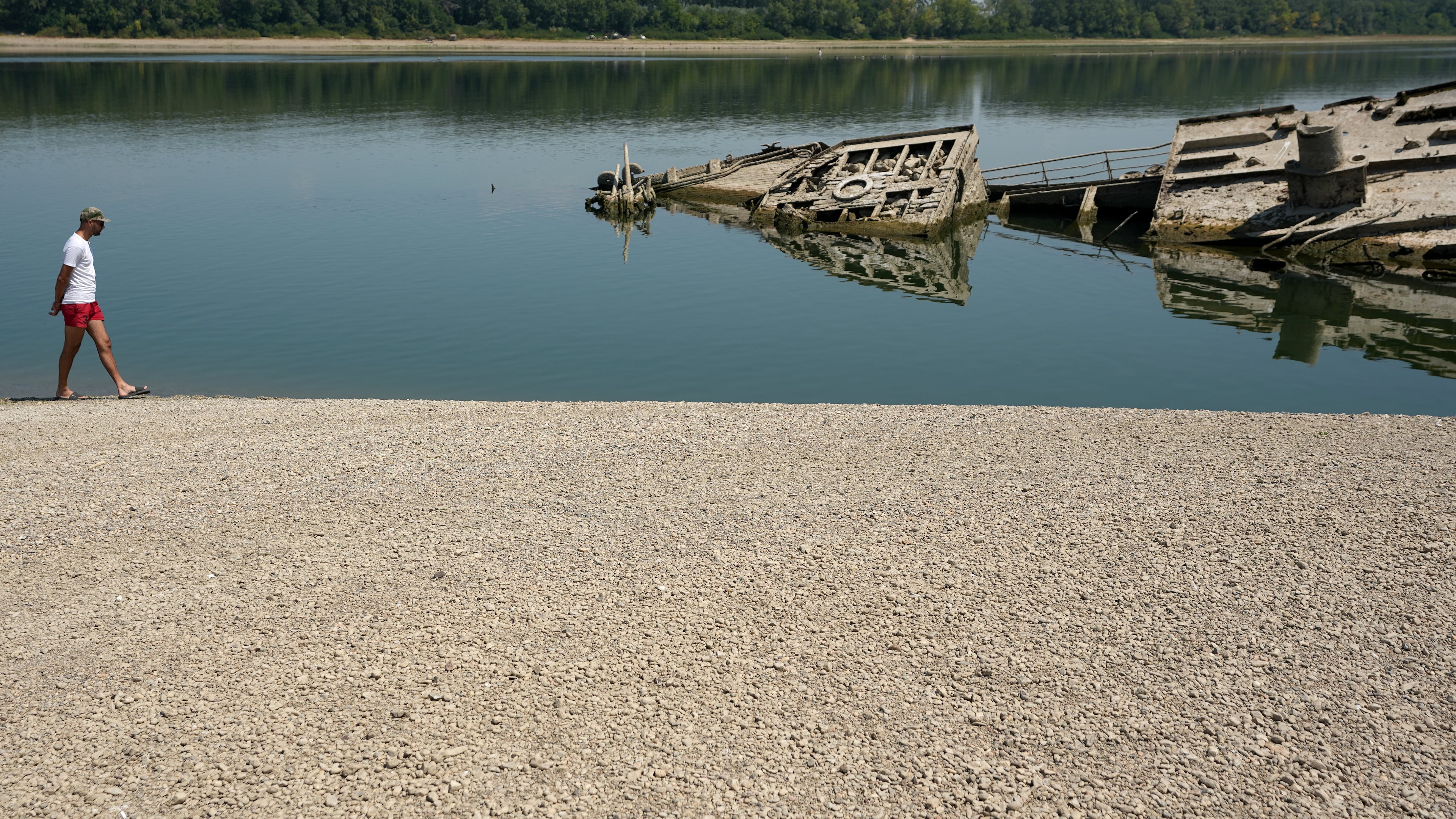 A man walks on the sandbank by the wreckage of a WWII German warship, emerged due to the drought, in front of Djerdap II, a large dam on the Danube River, between Romania and Serbia, near Prahovo, Serbia, Tuesday, Aug. 4, 2026. (AP Photo/Darko Vojinovic)