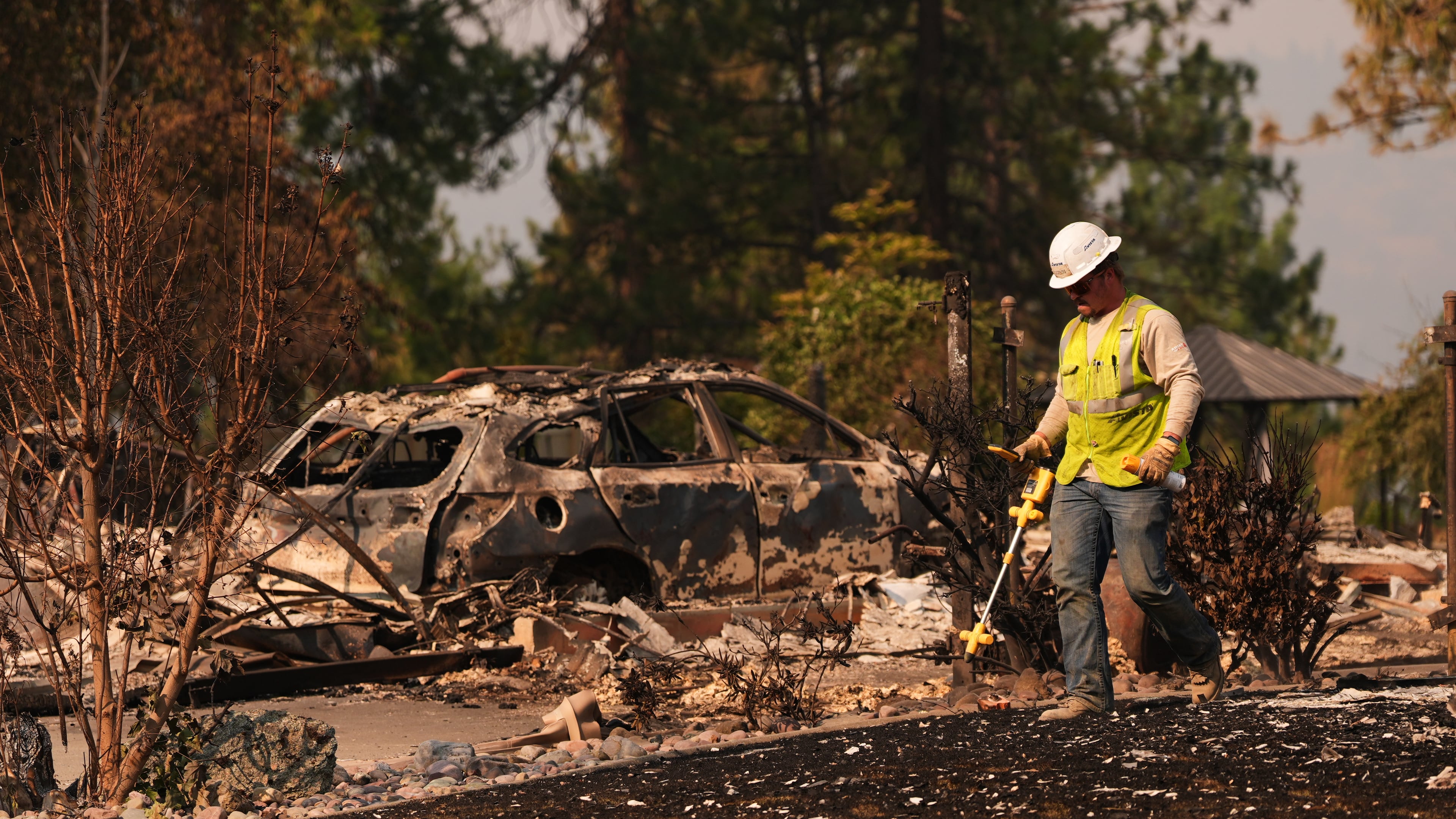 A worker with Avista moves through a property after a wildfire hit the northern part of Spokane, Wash., Monday, Aug. 3, 2026. (AP Photo/Lindsey Wasson)
