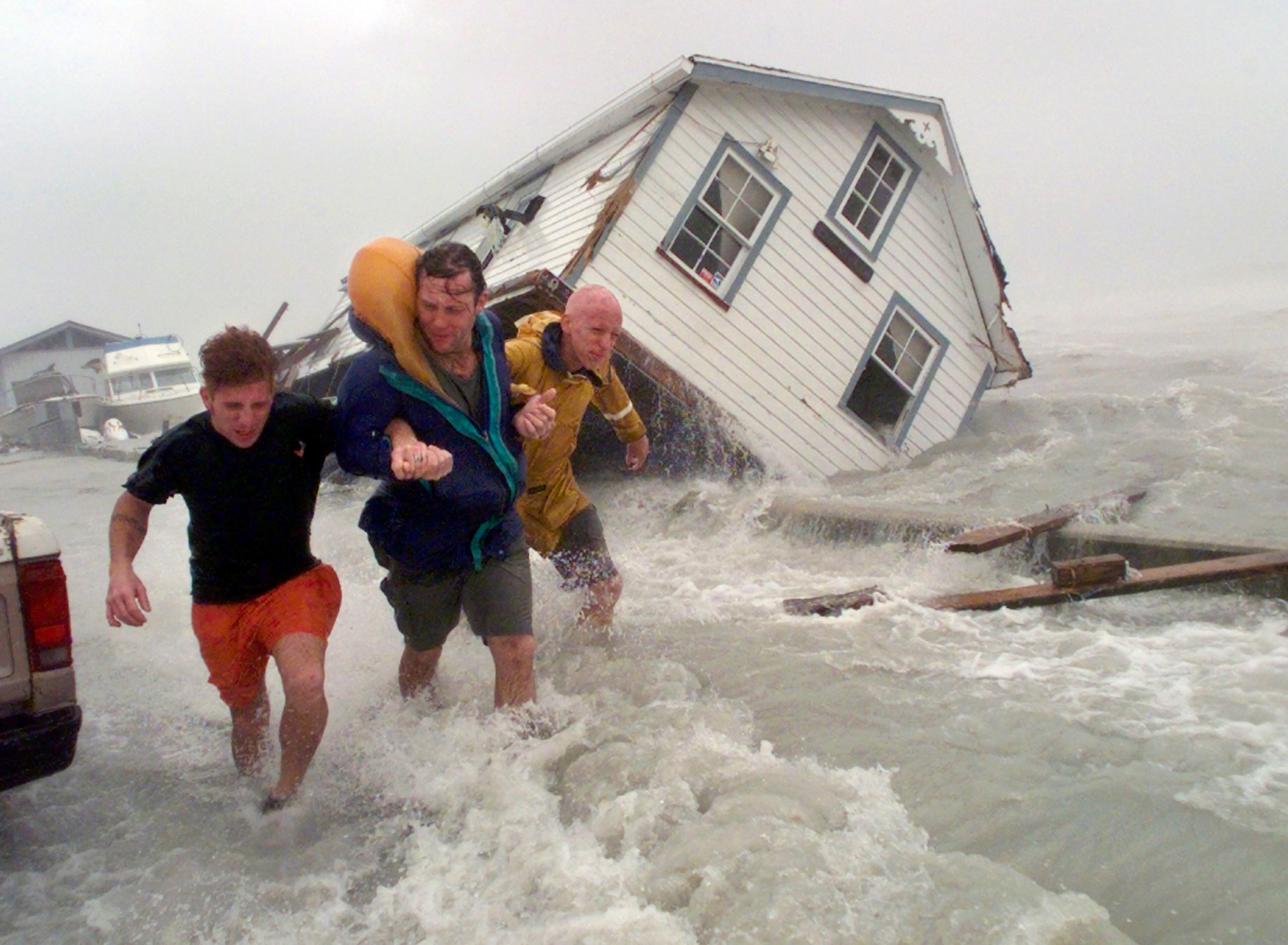 In this Sept. 25, 1998 file photo, taken by Dave Martin, Key West residents Brian Goss, left, George Wallace and Michael Mooney, right, hold on to each other as they battle 90 mph winds along Houseboat Row in Key West, Fla., after the three had sought shelter behind a Key West hotel as Hurricane Georges descended on the Florida Keys. They were forced to seek other shelter when the storm conditions became too rough. Martin, a longtime Associated Press photographer based in Montgomery, Ala., died after collapsing on the Georgia Dome field at the Chick-fil-A Bowl footballg ame on Tuesday, Dec. 31, 2013. Martin was 59. (AP Photo/Dave Martin, File)