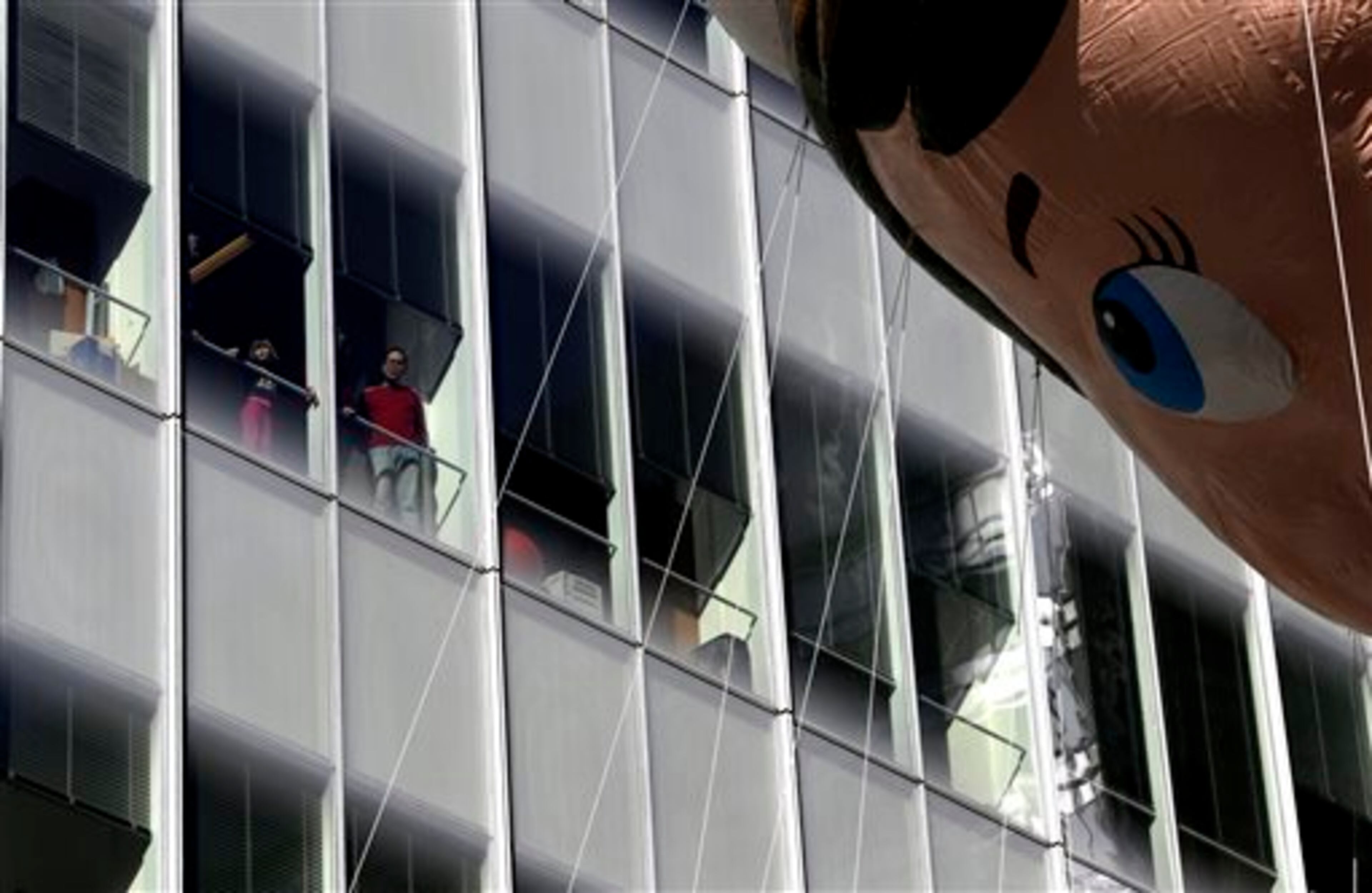 People look out of a window of a building as the Elf in a Shelf balloon flies by during the Macy's Thanksgiving Day Parade, Thursday, Nov. 28, 2013, in New York. (AP Photo/Julio Cortez)