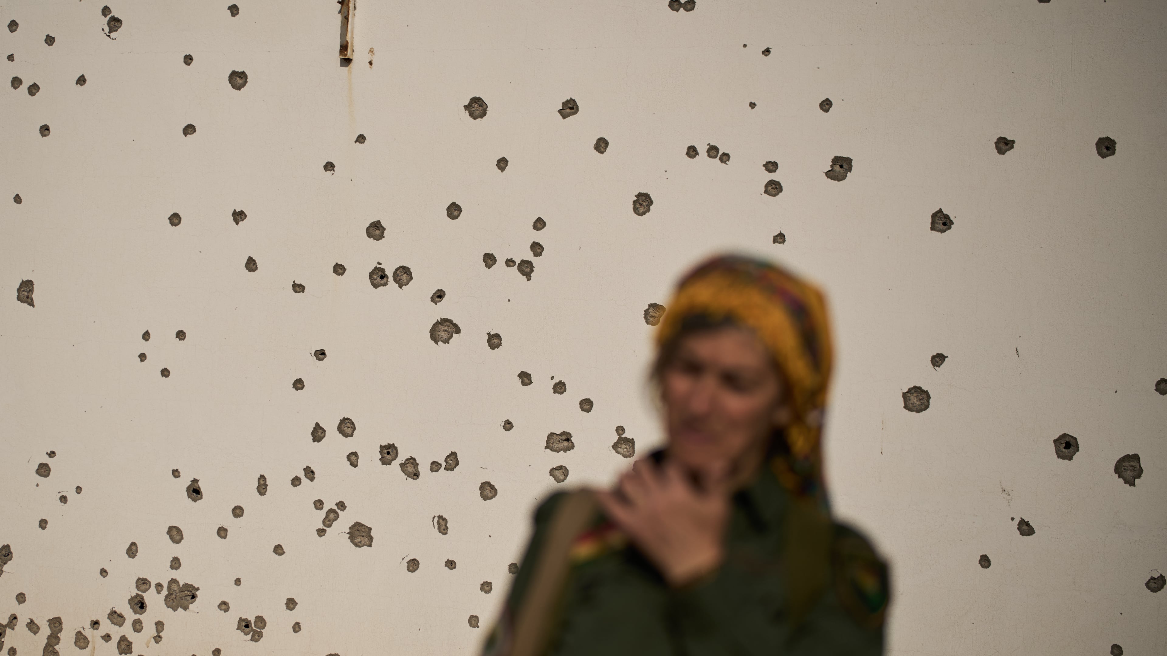 A member of the armed wing of the Kurdish-Iranian opposition group Organization of Iranian Kurdistan Struggle, known as Khabat, stands in front of a shrapnel pockmarked wall that allegedly was damaged in strike by Iranian-backed militias in Iraq last week at a military base on the outskirts of Irbil, Iraq, Monday, March 16, 2026. (AP Photo/Leo Correa)