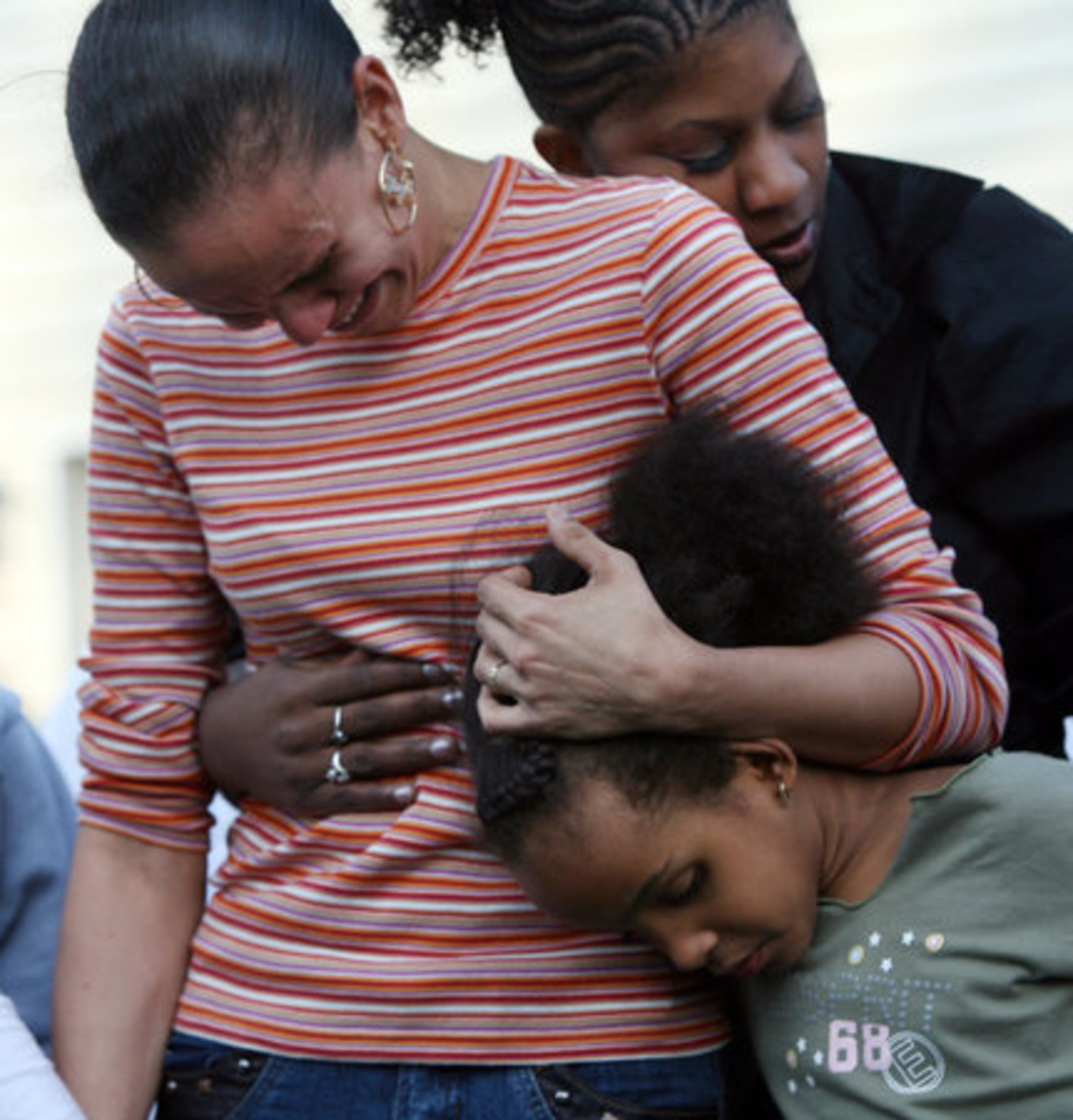 Masika Bermudez embraces her 5-year-old daughter Ny'irah and is comforted by family friend Angelic Mitchell, back, as she is joined by family and friends in a "prayer circle" to remember her fifth-grade son.