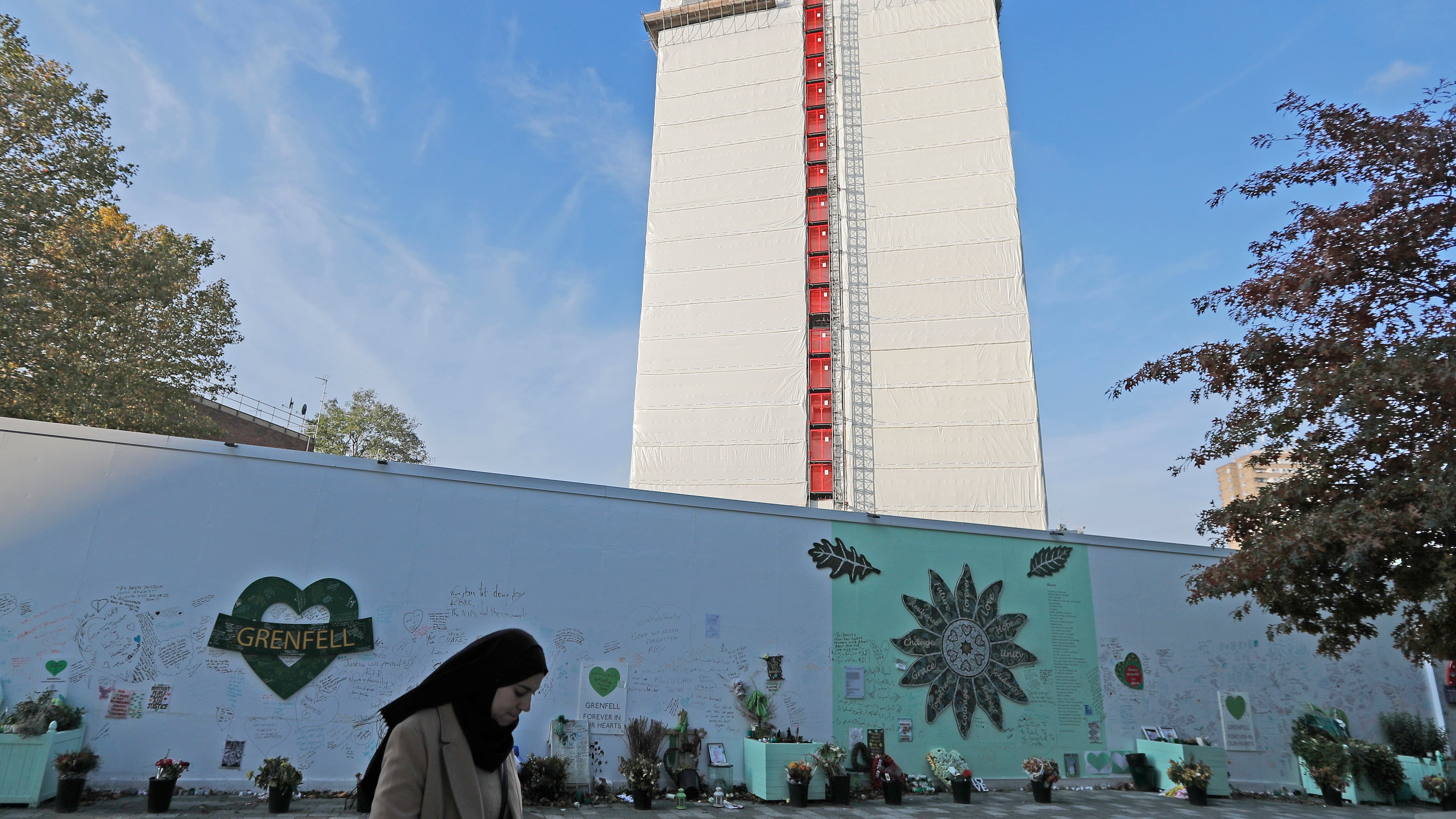 FILE - A woman passes a construction wall with written messages near Grenfell Tower in London, Wednesday, Oct. 30, 2019. (AP Photo/Frank Augstein, file)