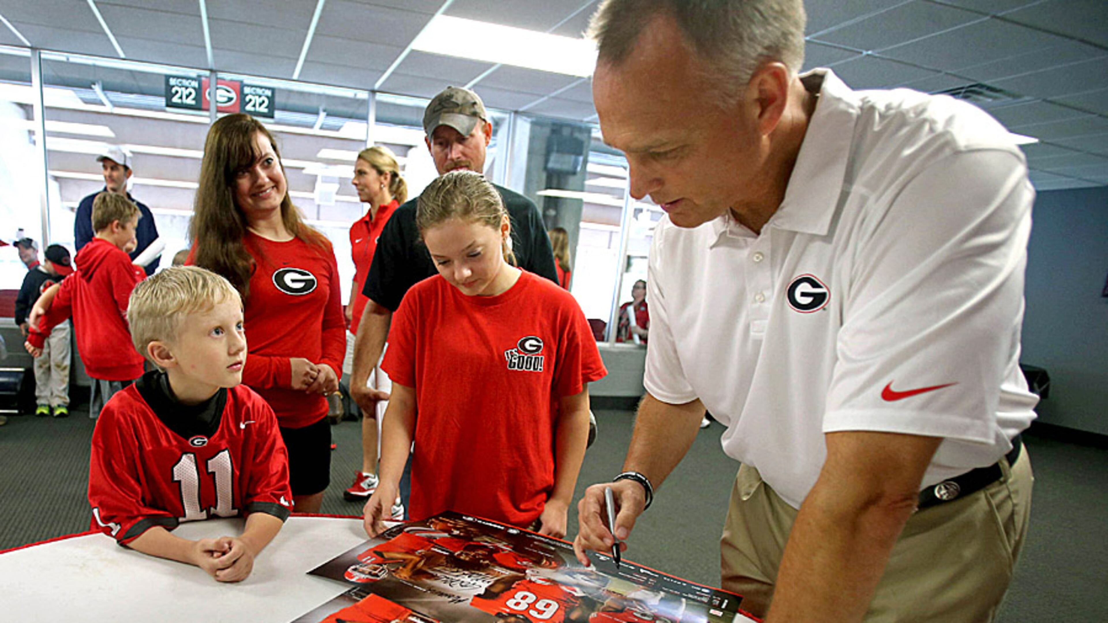 August 17, 2013 - Athens, Ga: University of Georgia coach Mark Richt, right, autographs a poster for Jaron Millican, 8, left, sister Michaela Millican, 13, mother Melanie Ward, top left, and father Shane Ward, of Gaylesville, during Georgia Fan Day at Sanford Stadium at the University of Georgia Saturday afternoon in Athens, Ga., August 17, 2013. JASON GETZ / JGETZ@AJC.COM