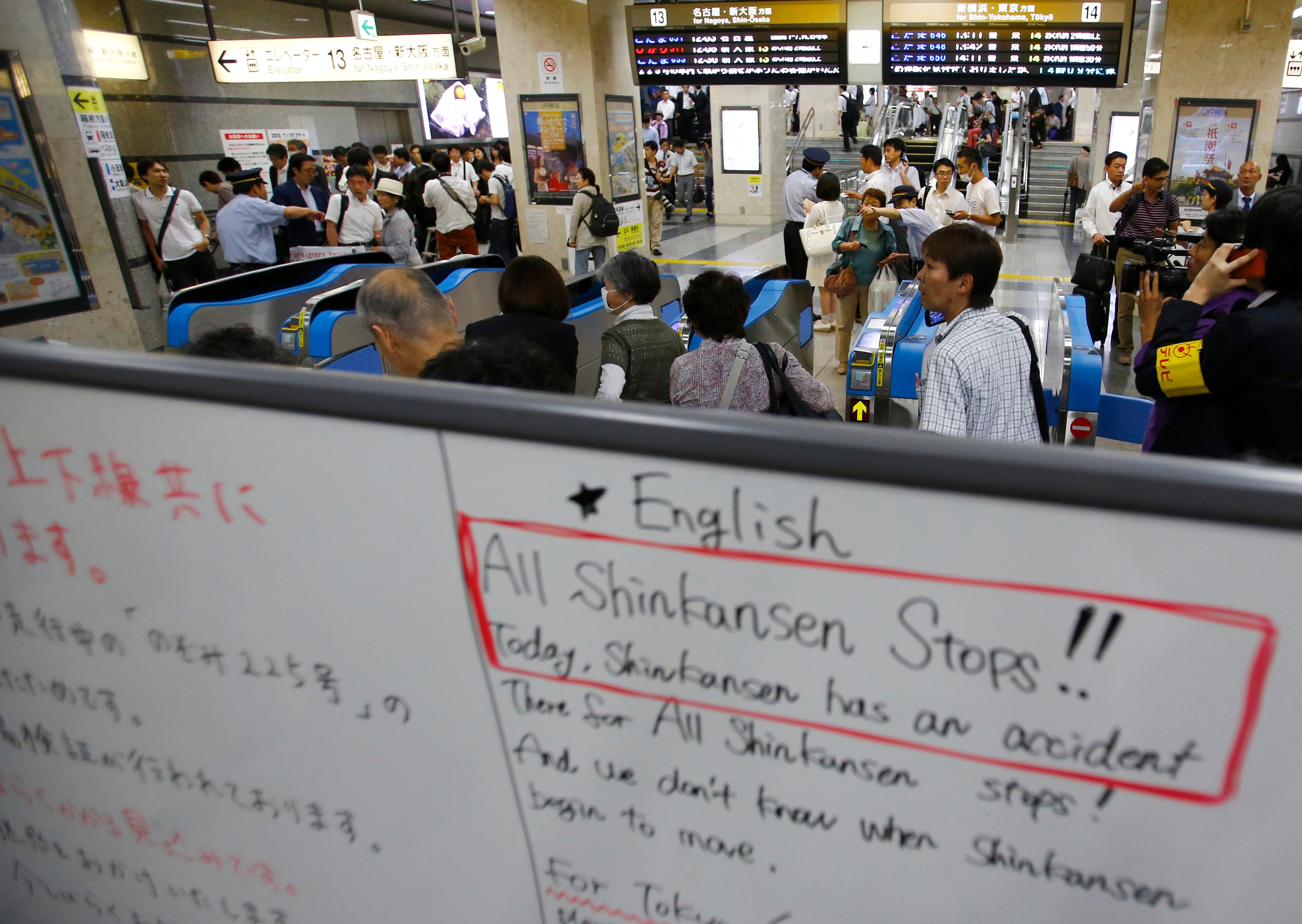 Passengers wait at an entrance to Odawara station in Odawara, west of Tokyo, after a man set himself on fire in a bullet train, Tuesday, June 30, 2015. The man riding one of Japan's high-speed bullet trains set himself on fire Tuesday, killing himself as the coach filled with smoke, Japanese officials and media reports said. The board in foreground reads: "All Shinkansen (bullet train) stops!" (AP Photo/Shizuo Kambayashi)