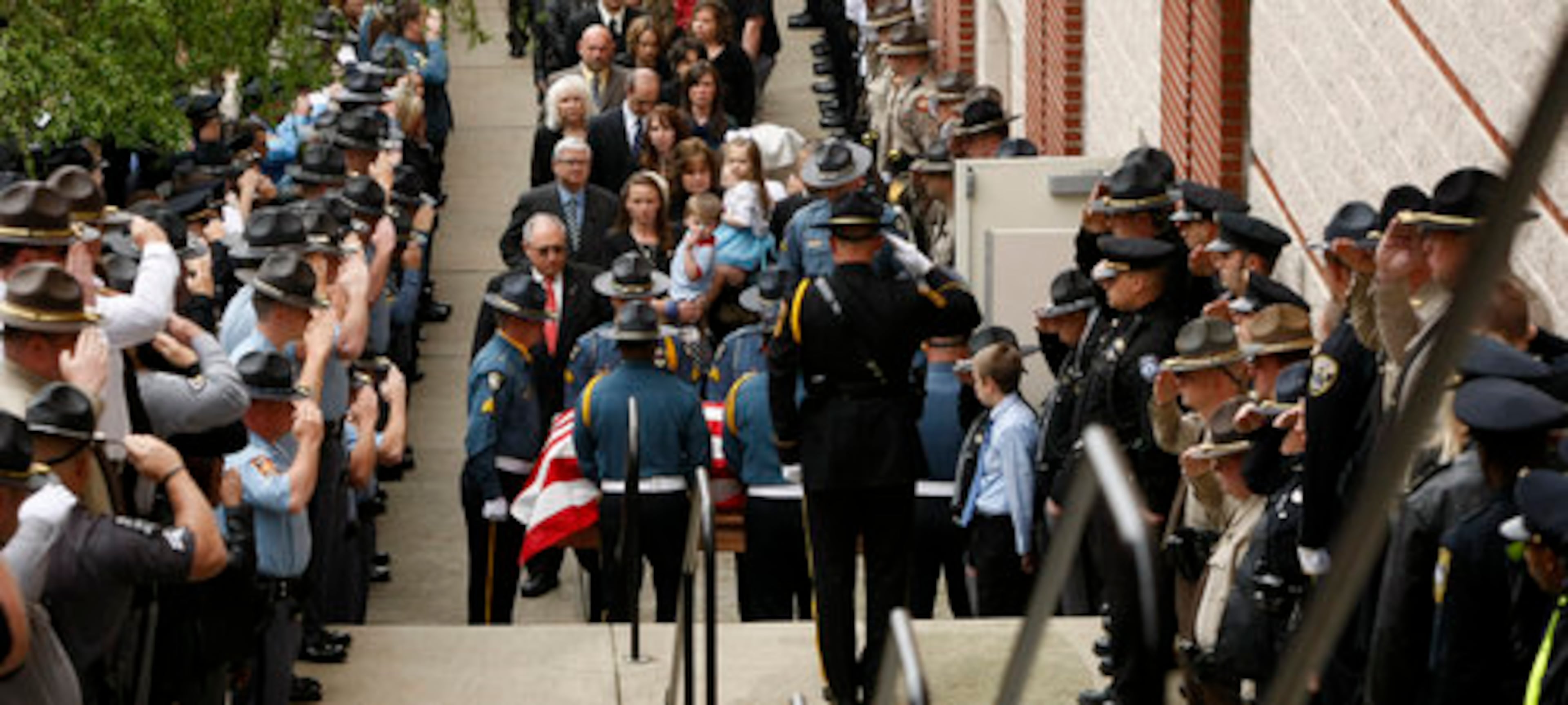 Law enforcement officers salute the flag-draped coffin of slain Athens Senior Officer Elmer "Buddy" Christian, followed by his wife and 2 children, as they arrive at the Classic Center Theatre in Athens on Sunday, March 27, 2011.