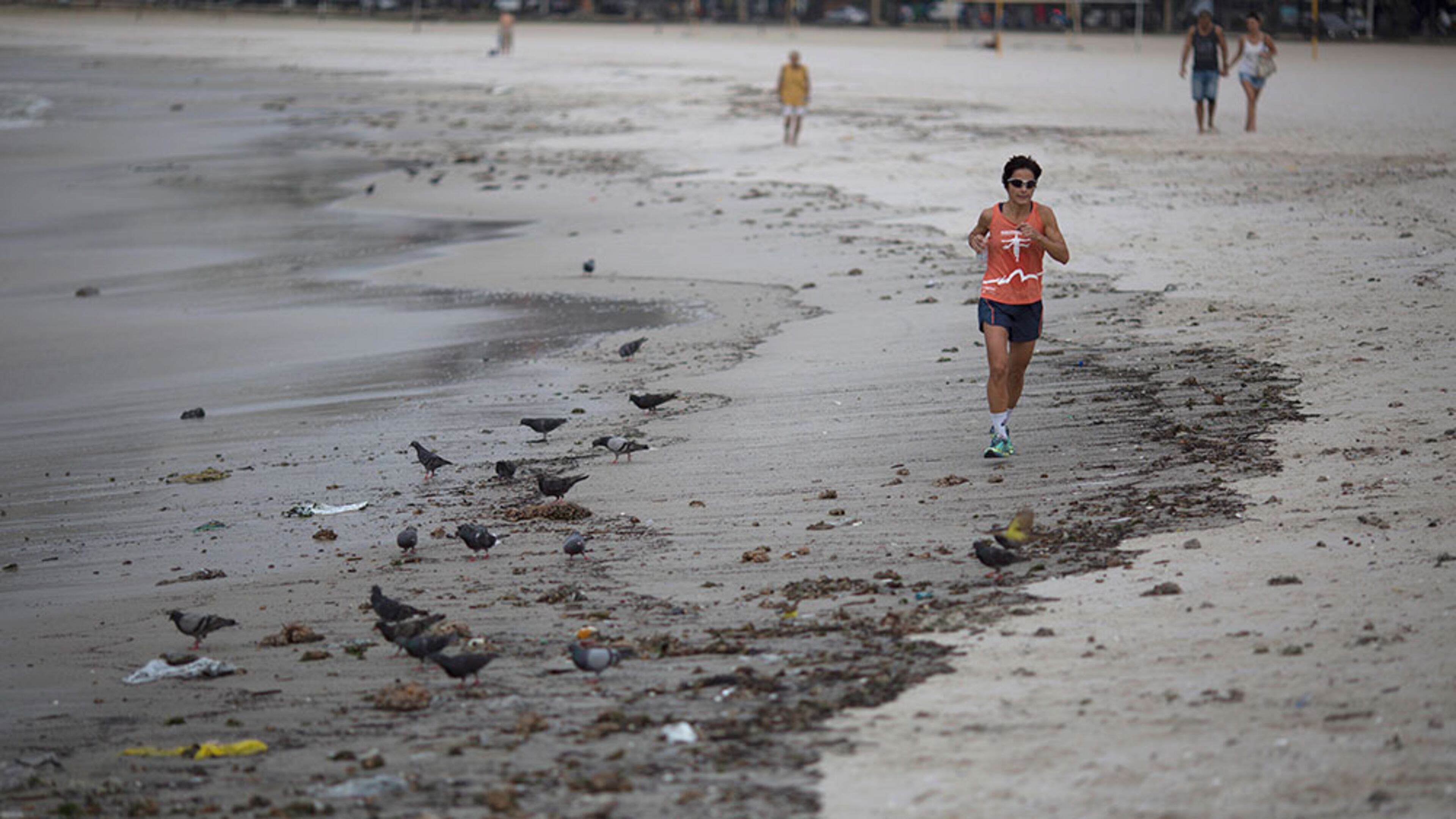 A woman runs next to the trash that litters the Botafogo beach next to the Sugar Loaf mountain and the Guanabara Bay in Rio de Janeiro, Brazil, Saturday, July 30, 2016. An Associated Press investigation has found the waters where Olympians will compete in swimming and boating events next summer in South America's first games are rife with human sewage and present a serious health risk for athletes.