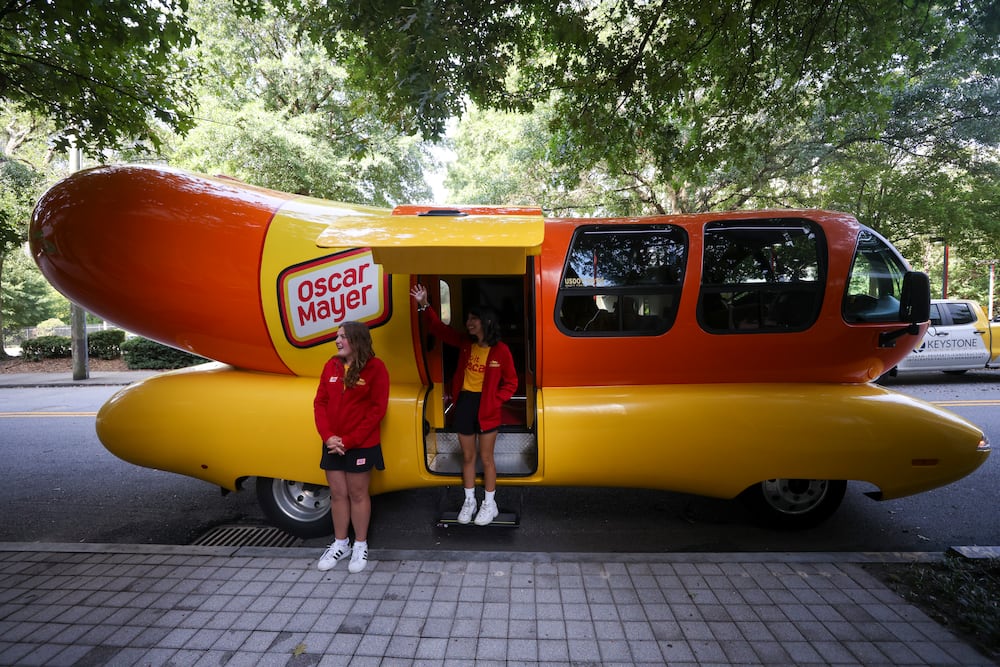 Hotdoggers Carly Bowden, left, and Evie Serda, center, greet the public after the Oscar Mayer Wienermobile toured the area, Tuesday, Aug. 18, 2026, in Atlanta. ("Jumbo Dog" Jason Getz/AJC)