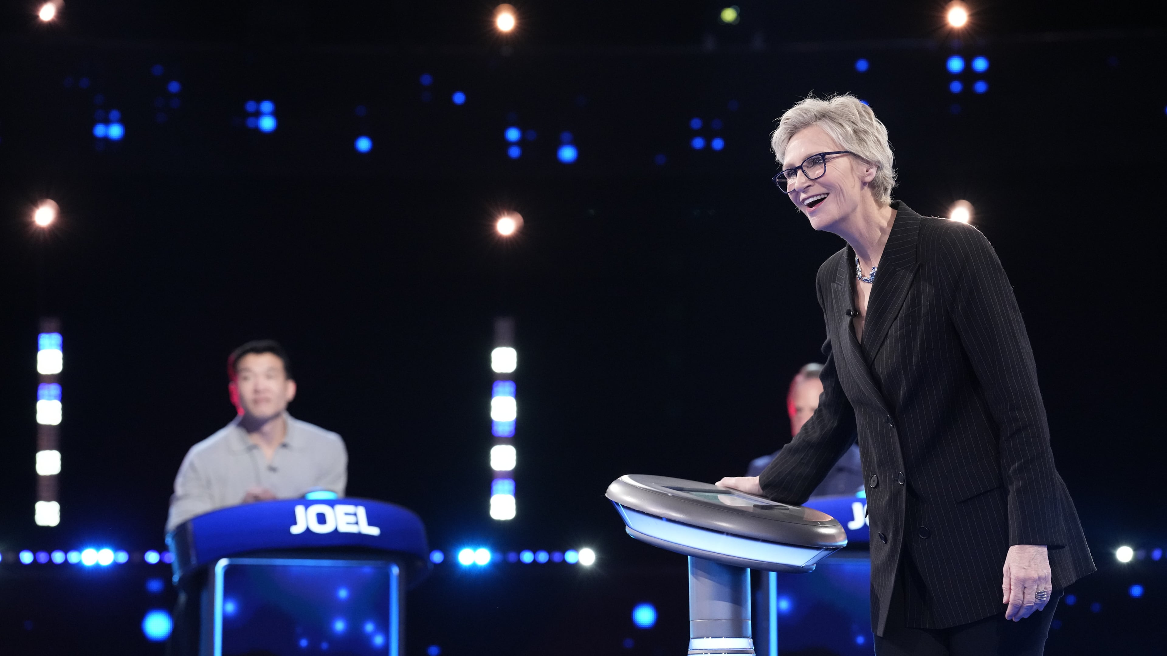 Jane Lynch (right) hosts as Joel Kim Booster competes on Fox’s “Celebrity Weakest Link.” The trivia game show is the latest in an array of primetime game shows coming to metro Atlanta. (Greg Gayne/Fox 2025)