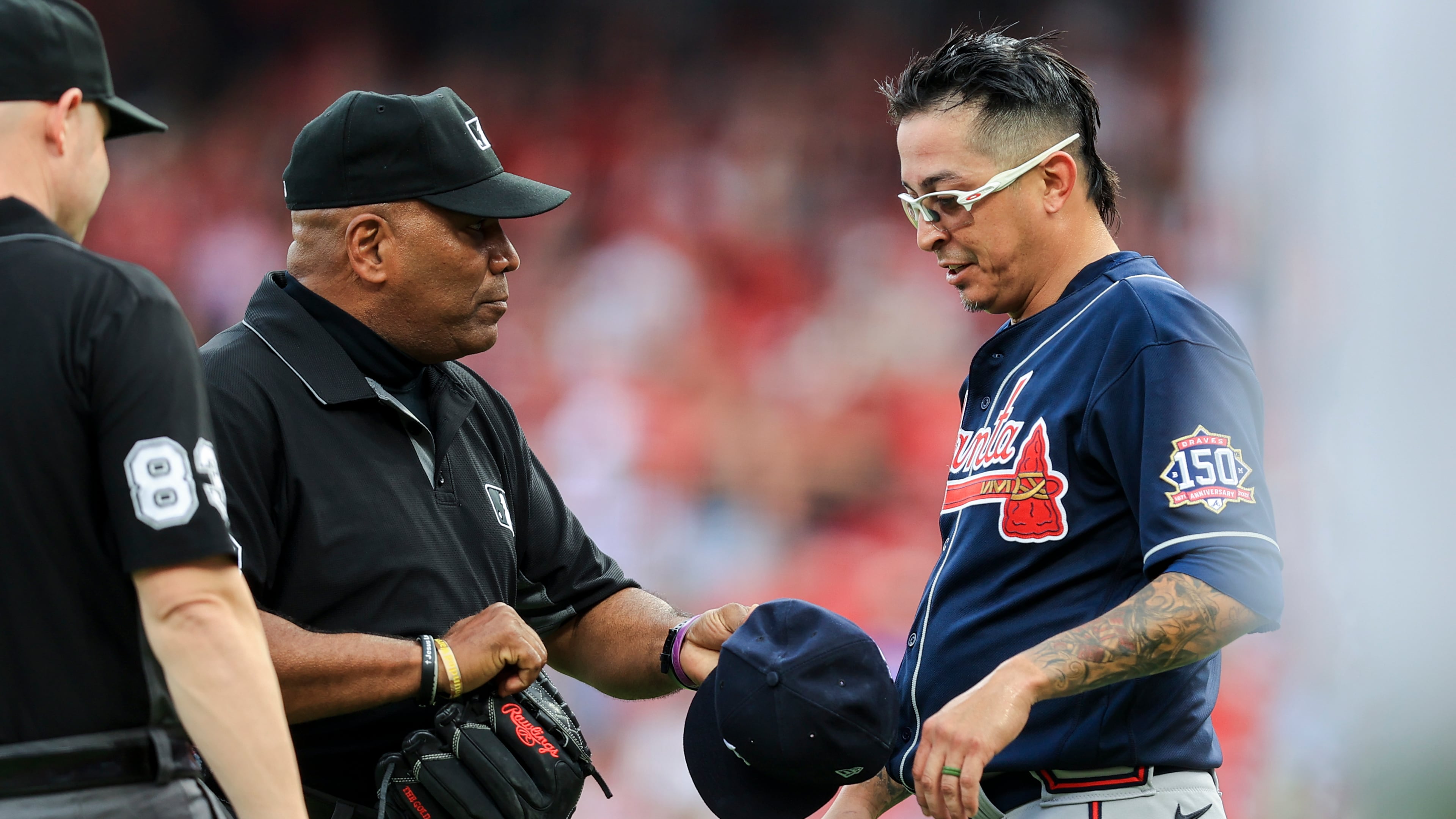 MLB umpire Laz Diaz, left, inspects the hat and glove of Atlanta Braves' Jesse Chavez after the first inning of a baseball game against the Cincinnati Reds in Cincinnati, Thursday, June 24, 2021. (AP Photo/Aaron Doster)