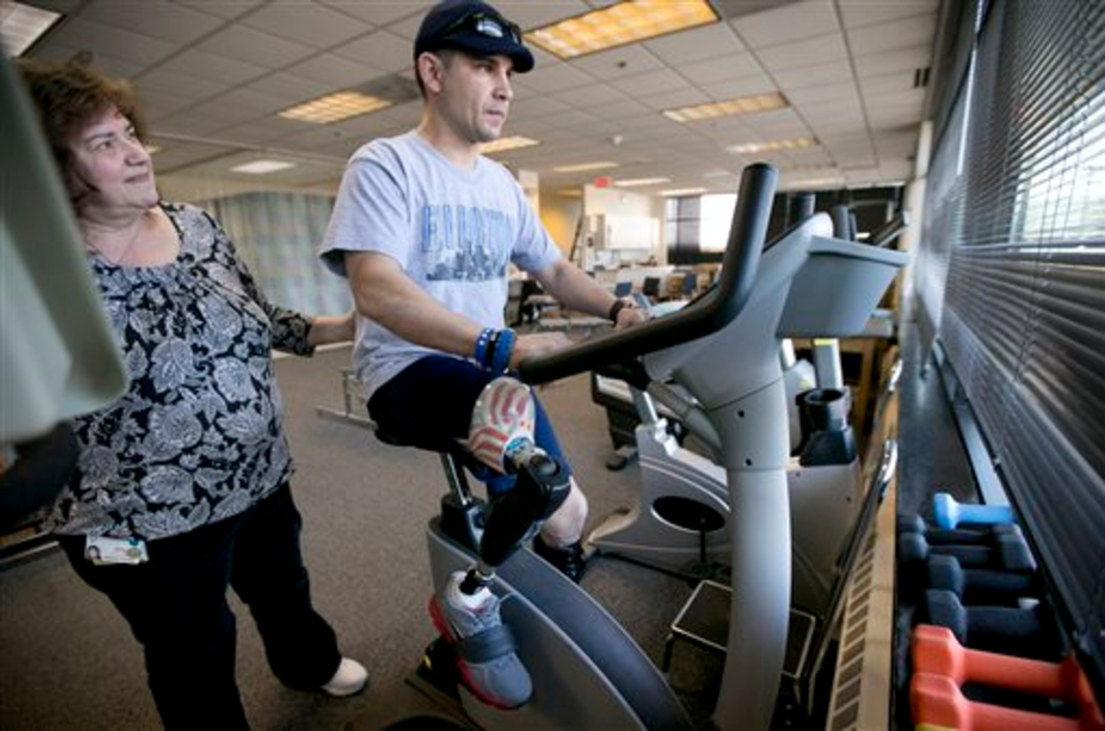 In this Thursday, April 3, 2014 photo, Boston Marathon bombing survivor Marc Fucarile, of Reading, Mass., right, is helped by physical therapy assistant Joy Ross, with rehabilitation exercises on a stationary bike at Spaulding Outpatient Center in Peabody, Mass. Fucarile lost his right leg in an explosion near the finish line of the 2013 race. (AP Photo/Steven Senne)