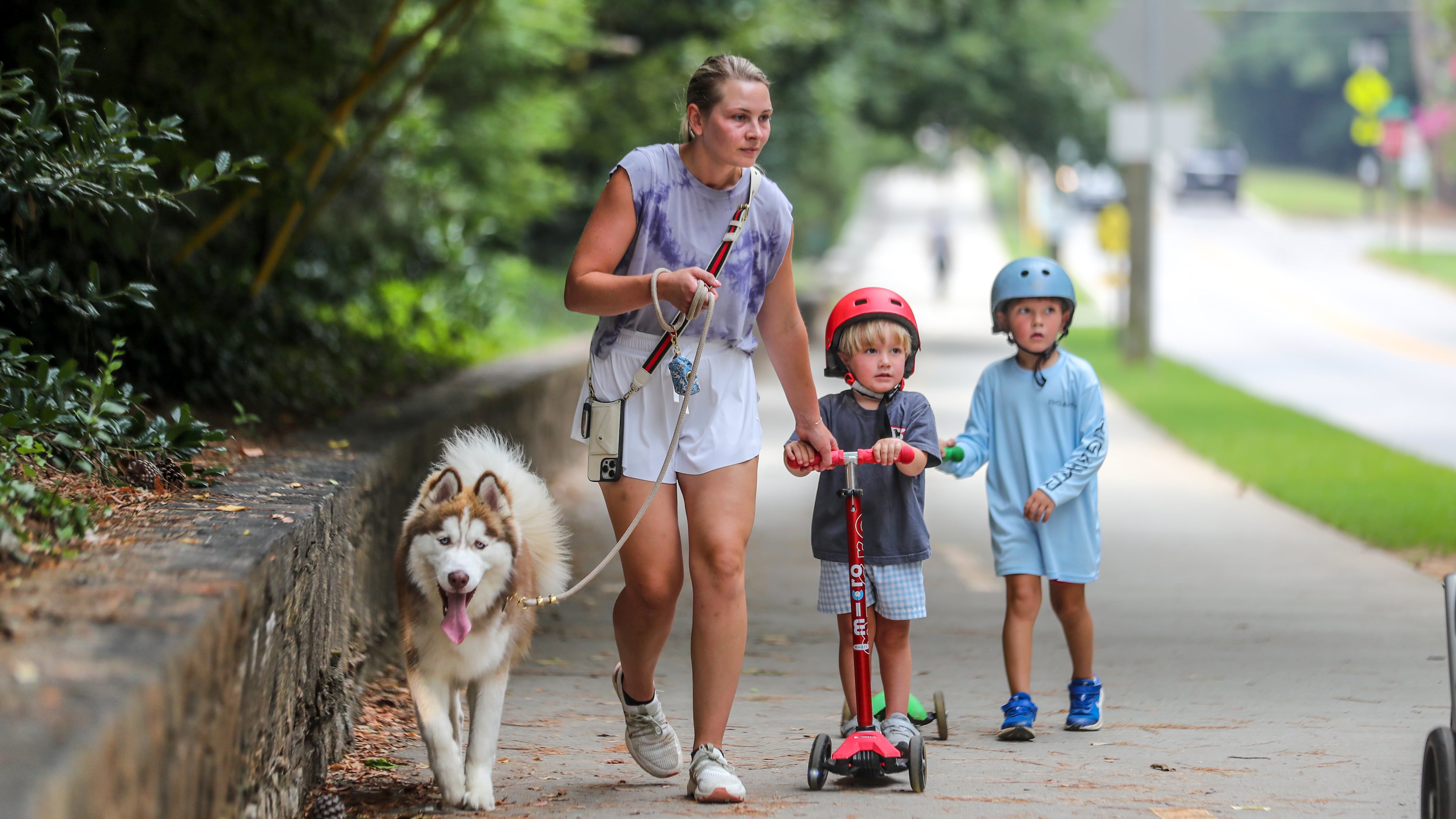 July 17, 2023 Atlanta: Madison Langston holds onto husky, Bosley (left) as 3-year old Charlie (center) and brother, Petey-4 (right) make their way along the long sidewalk at Chastain Park in Atlanta on Monday, July 17, 2023. (John Spink / John.Spink@ajc.com)