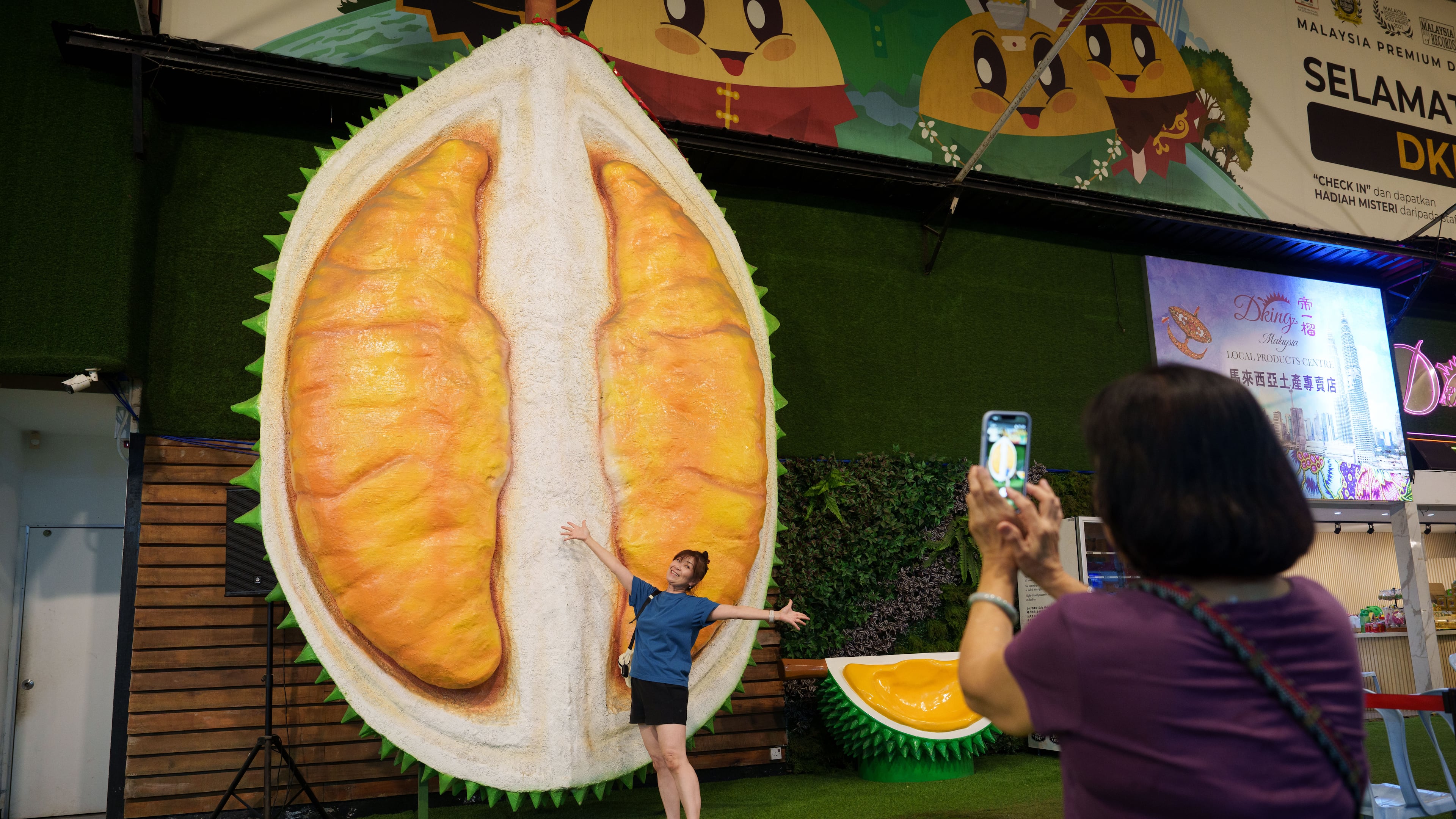A customer poses beside a giant durian display at a durian stall in Petaling Jaya, on the outskirts of Kuala Lumpur, Malaysia, Monday, June 22, 2026. (AP Photo/Vincent Thian)