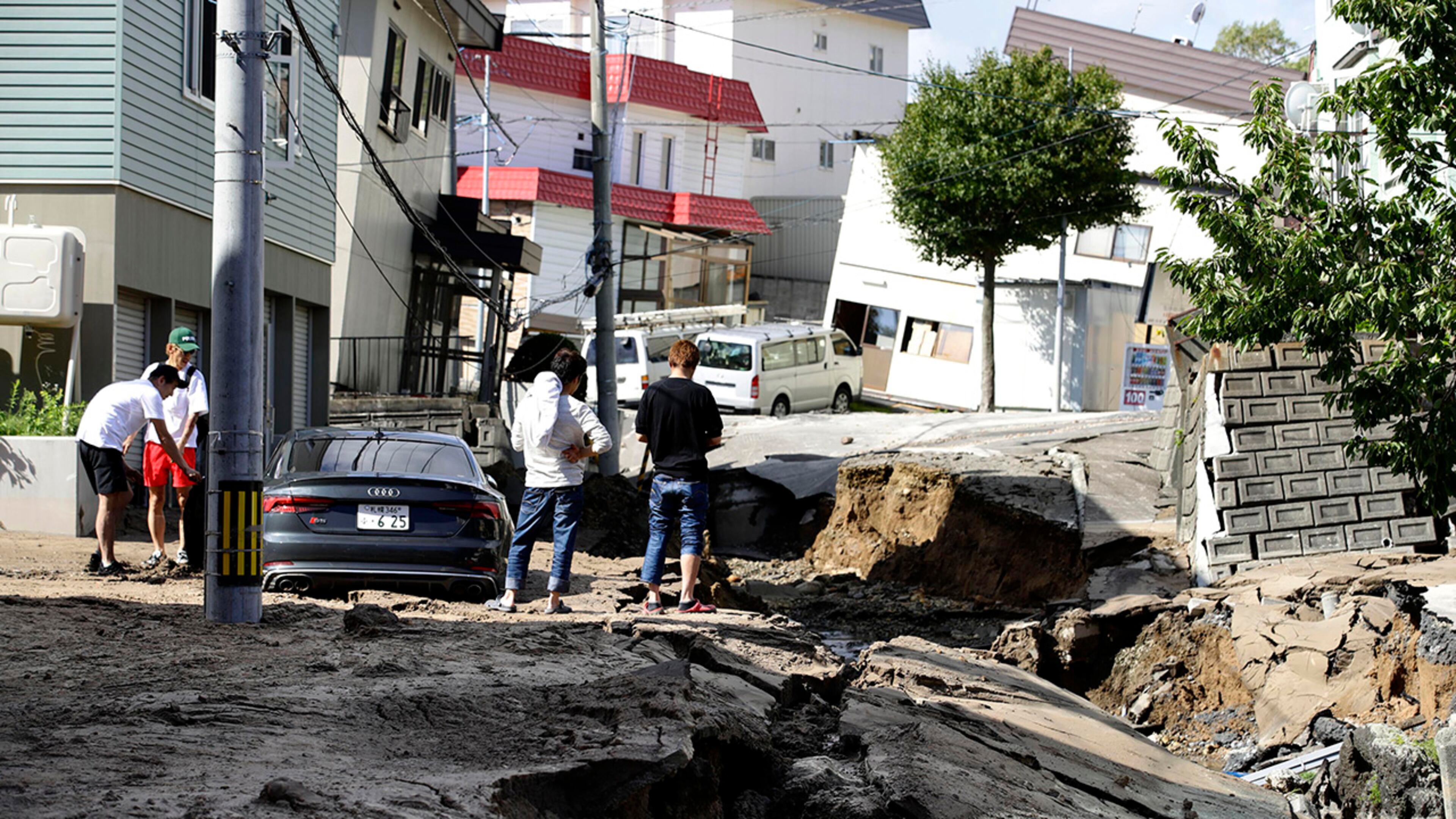 Residents watch a road damaged by an earthquake in Sapporo, Hokkaido, northern Japan, Thursday, Sept. 6, 2018. A powerful earthquake shook Japan's northernmost main island of Hokkaido early Thursday, causing landslides that crushed homes, knocking out power across the island. (Hiroki Yamauchi/Kyodo News via AP)