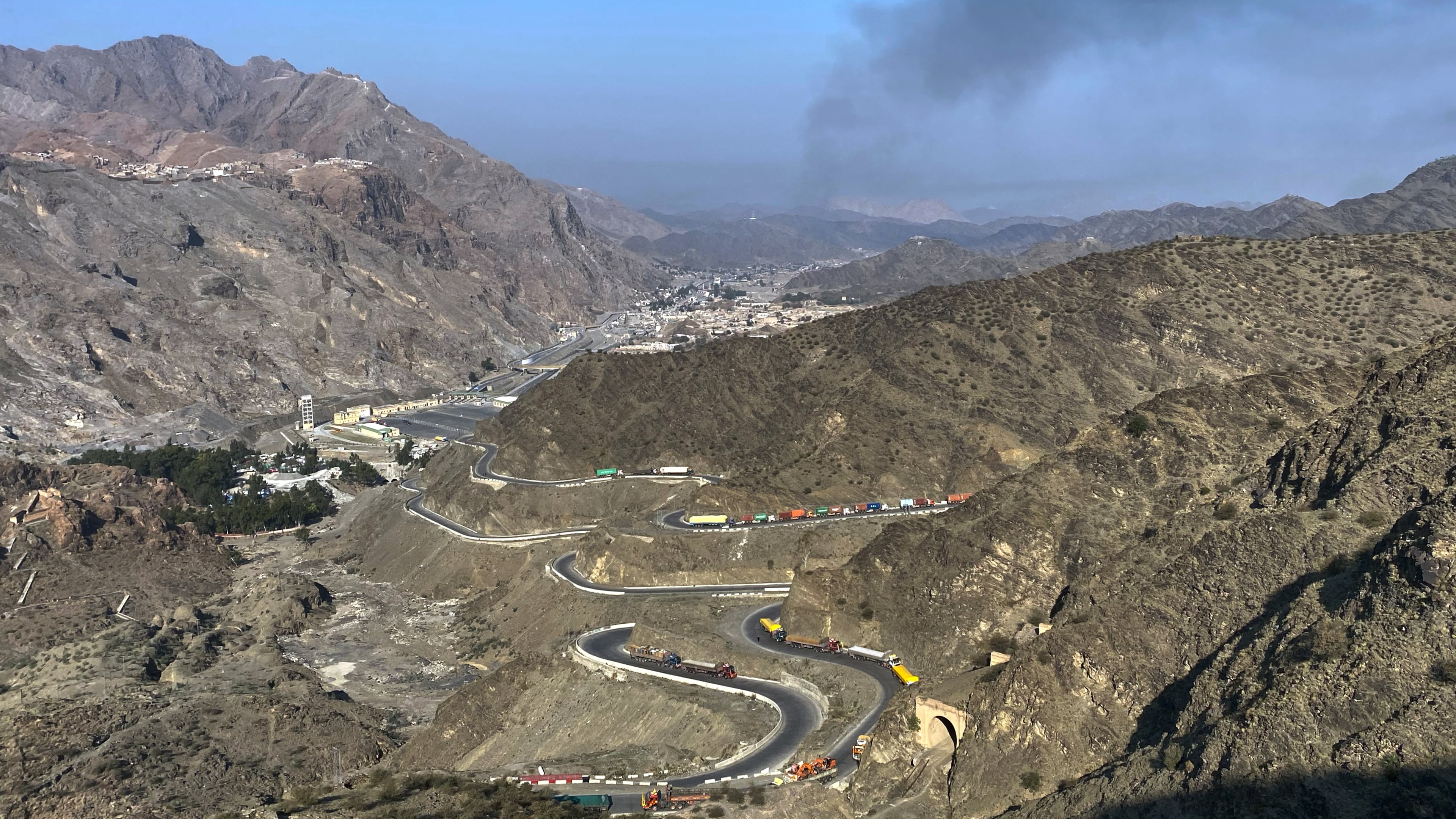 Smoke emits from Afghan side as trucks are parked along roadside following cross-border clashes between Pakistan and Afghan forces, at near Torkham border crossing point, Pakistan, Saturday, Feb. 28, 2026. (AP Photo/Maaz Awan)